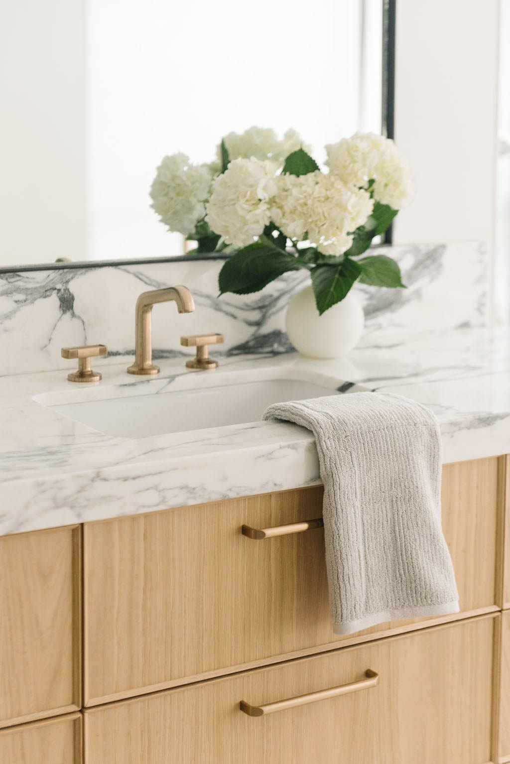 Ribbed Terry Hand Towels in the color Light Grey. Photo of product taken with the product draped over a white marble sink. 