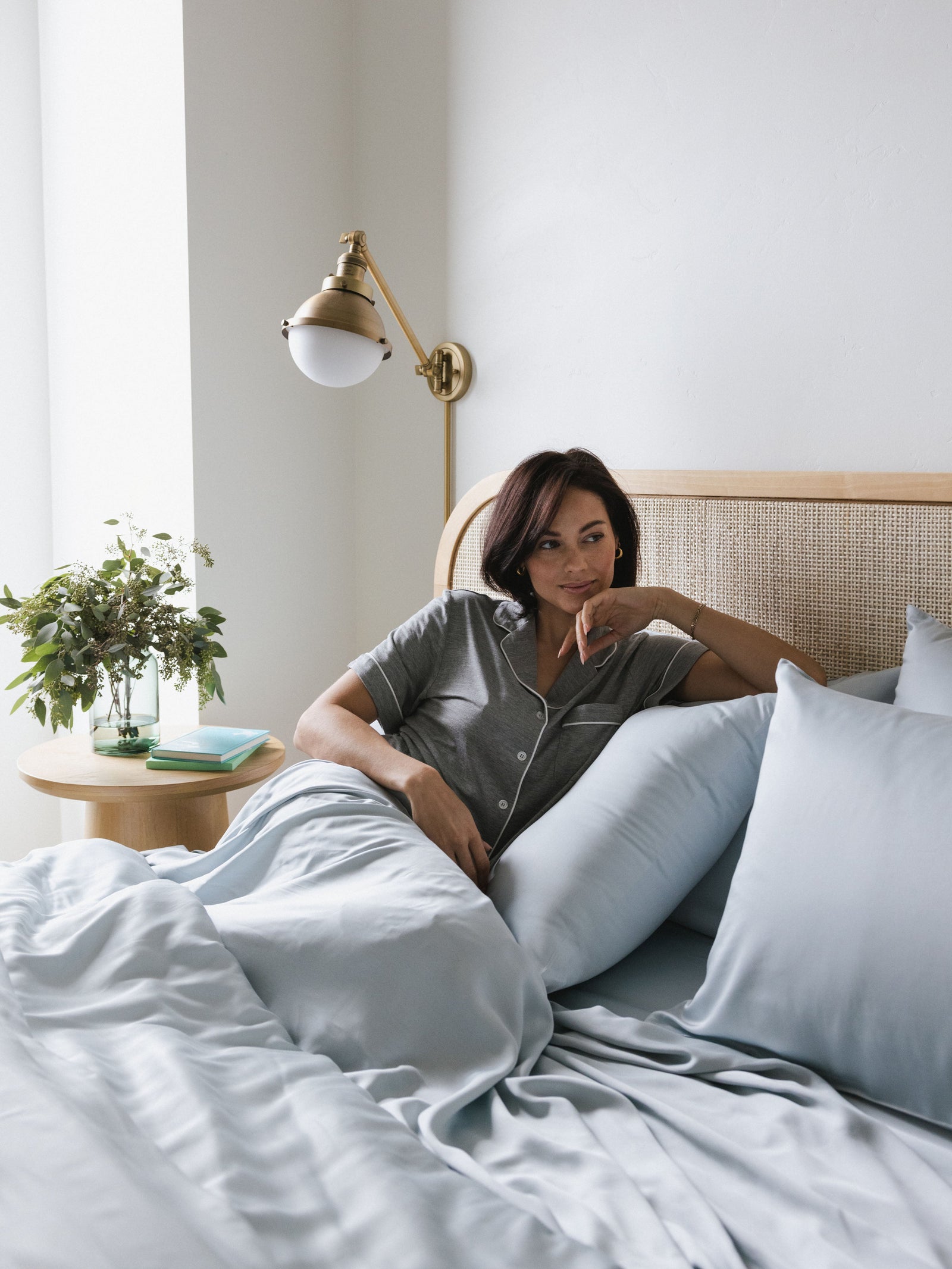 Woman in grey pajamas laying in bed with shore bedding 