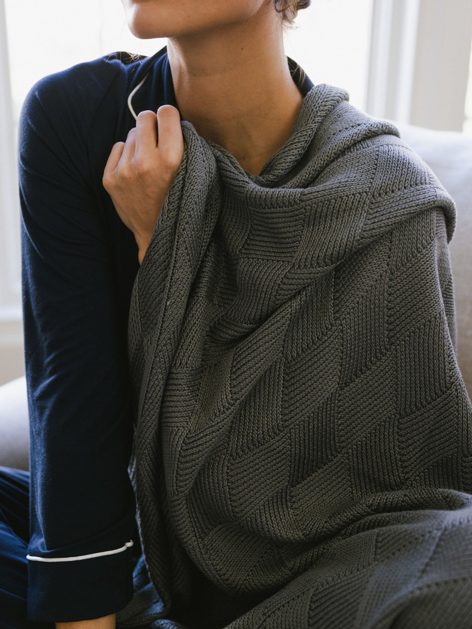 Stone Diamond Knit Blanket photographed in a home living room. A woman holds the blanket over her shoulder. 
