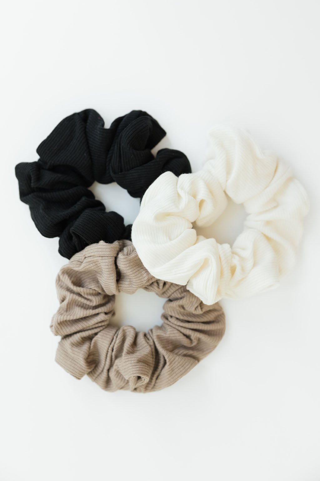 Three scrunchies in black, beige, and white on a white background