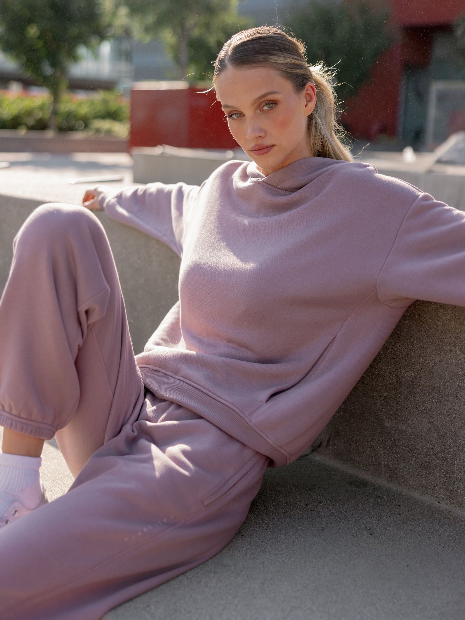 Woman sitting on bench wearing dusty orchid cityscape hoodie and sweats 