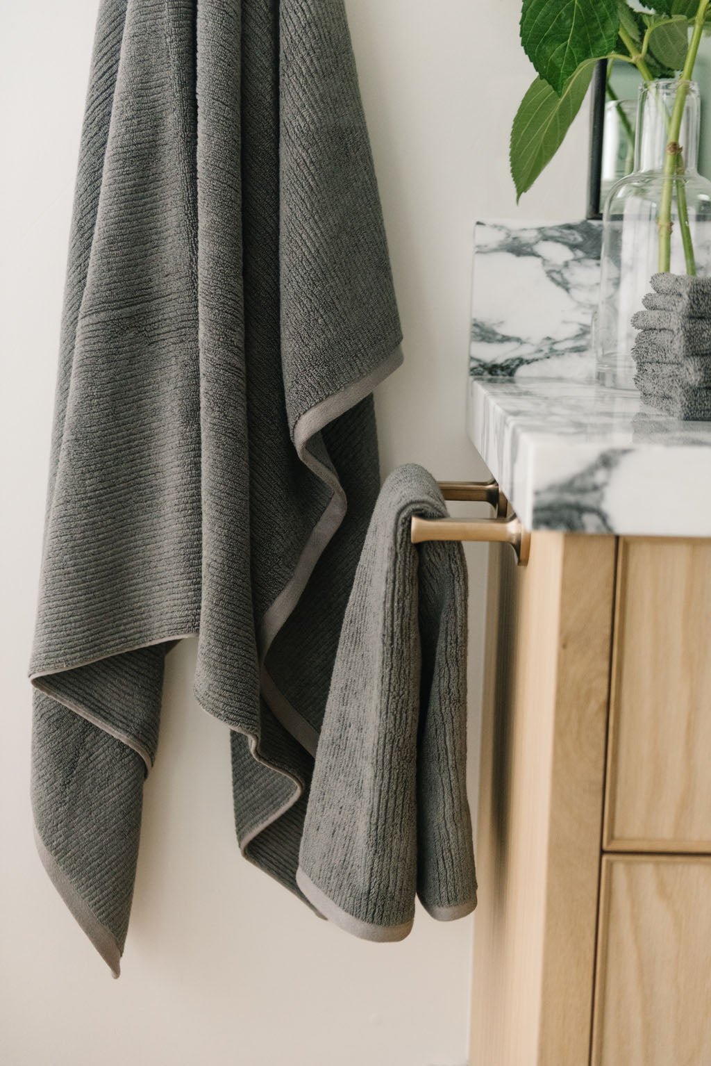 Ribbed Terry Hand Towels in the color charcoal. Photo of product taken with the product draped over a towel bar on the side of a white marble sink. 