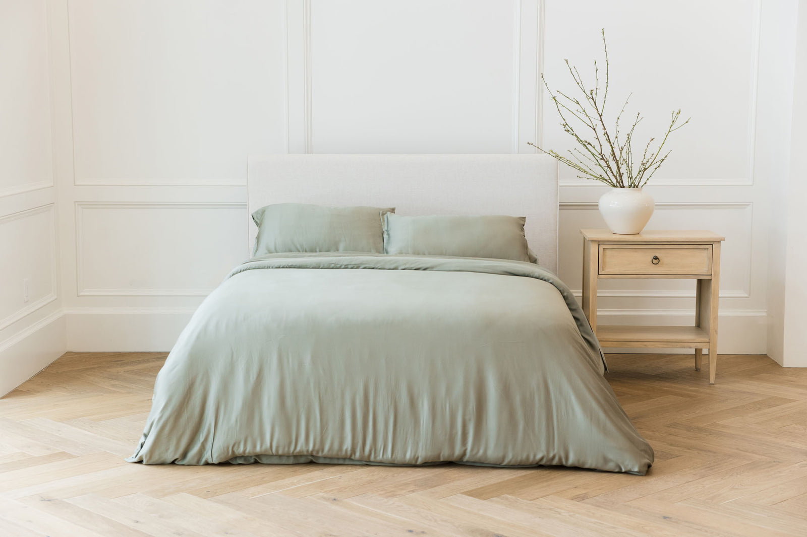 Bed with sage bedding centered in a bedroom