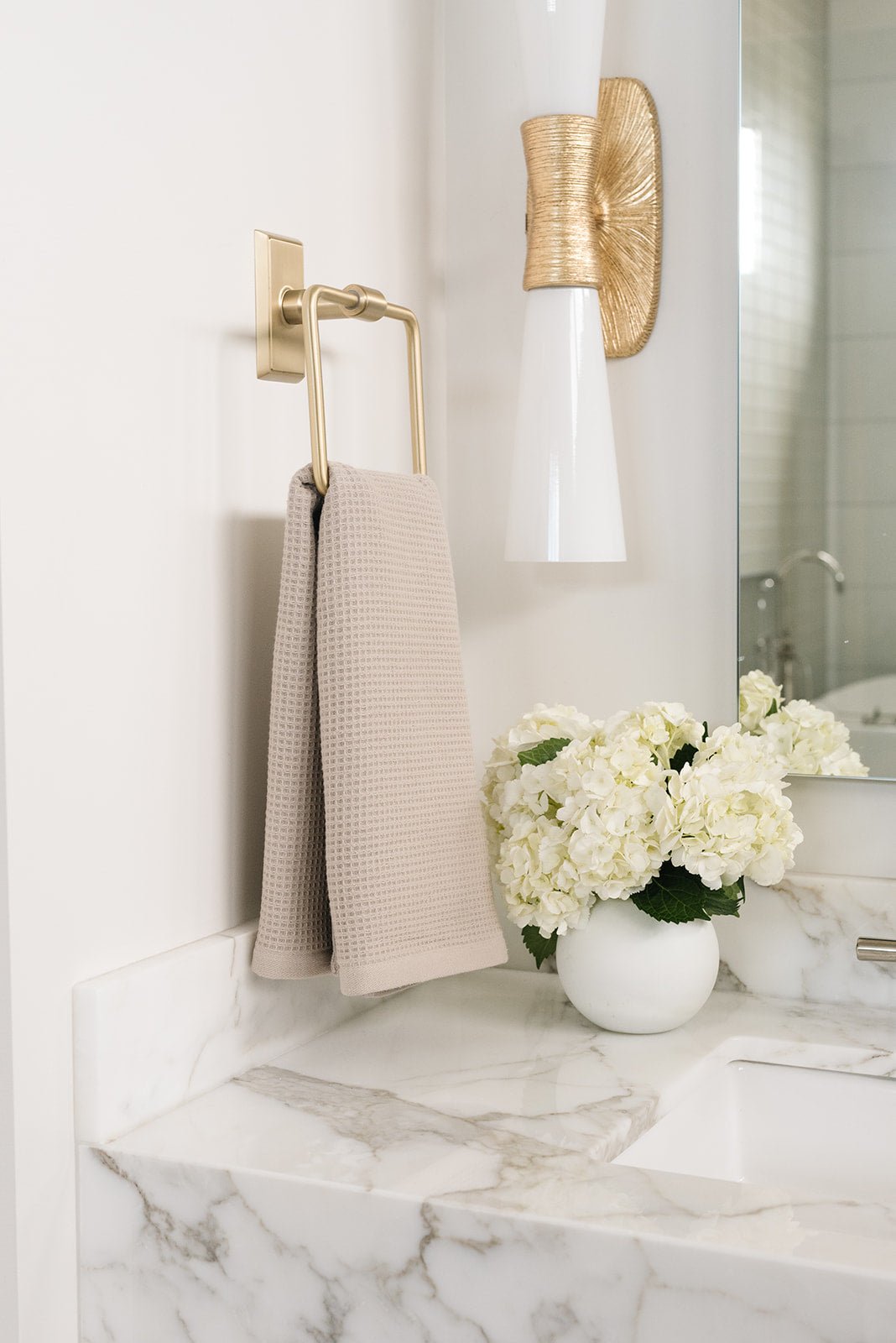 Sand Waffle Hand Towel hanging from a gold towel ring.  The photo was taken at a white marble bathroom sink. 