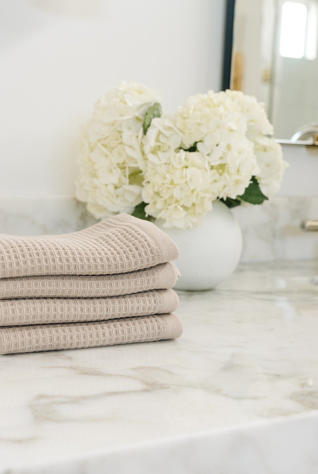 Sand Waffle Wash Cloths neatly folded. The photo was taken with the cloths resting on a white marble sink. 