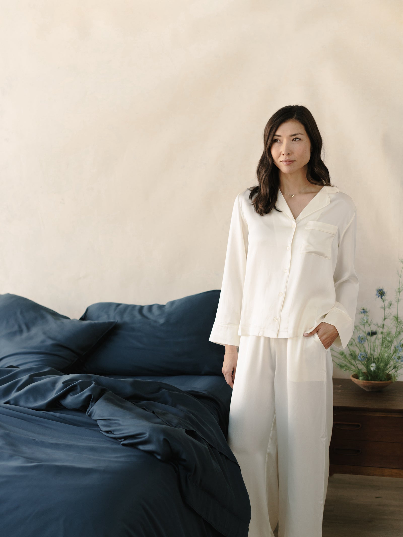 Woman in pajamas standing next to a bed with navy bedding 