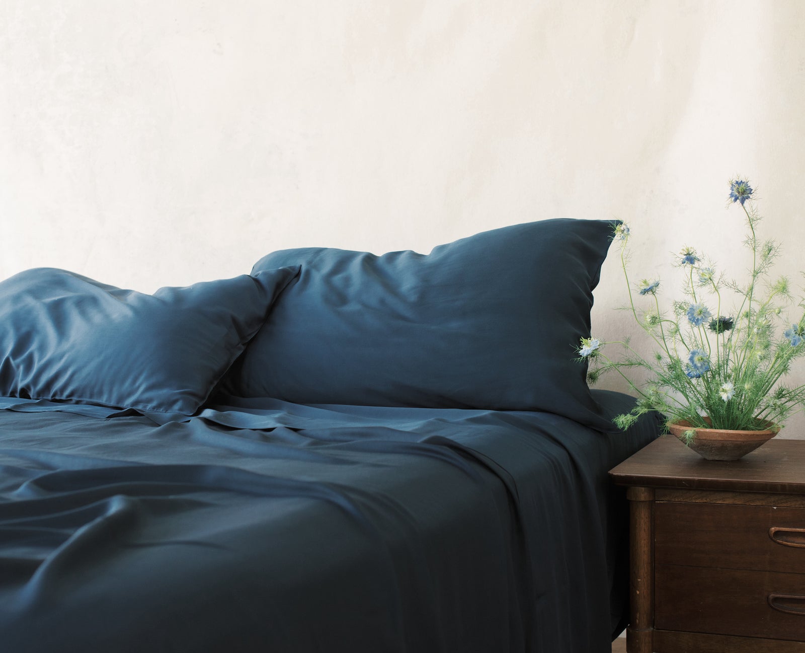 Unmade bed with navy bedding and flowers on nightstand 