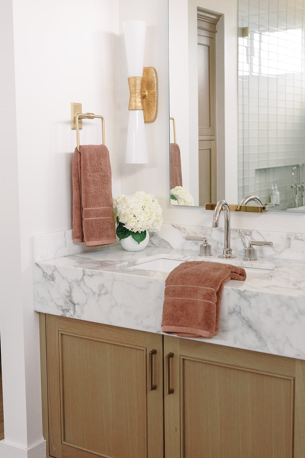 Premium Plush Hand Towel in the color Clay. Photo of Clay Premium Plush Hand Towel taken in a bathroom. One Premium Plush Hand Towel is hanging from a towel ring while the other is resting on the sink in the bathroom.