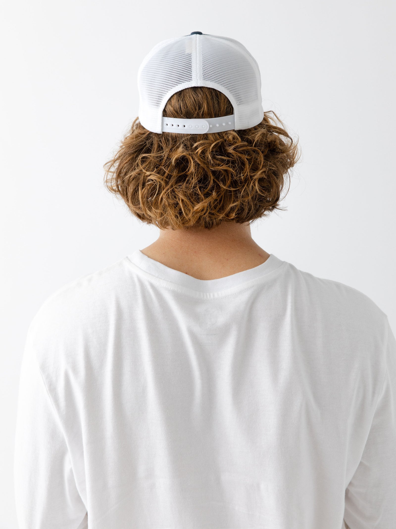 Man facing backwards wearing a Navy and white cap with a CE logo on a light gray background