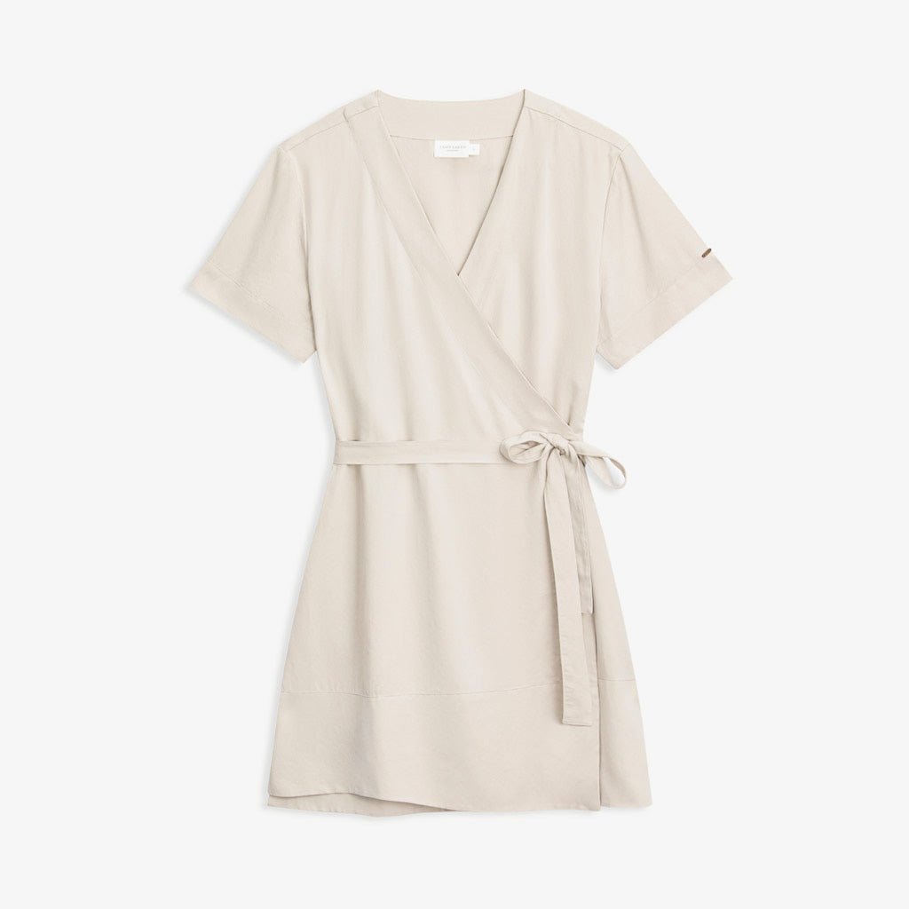 The Women's Cozy Earth Coastal Comfort Wrap Dress by Cozy Earth is laid flat against a white background. This light beige short-sleeved dress features a V-neckline and a waist tie belt made of the same fabric, designed to be tied at the side. It boasts a smooth, soft-looking texture with a simple and elegant style.