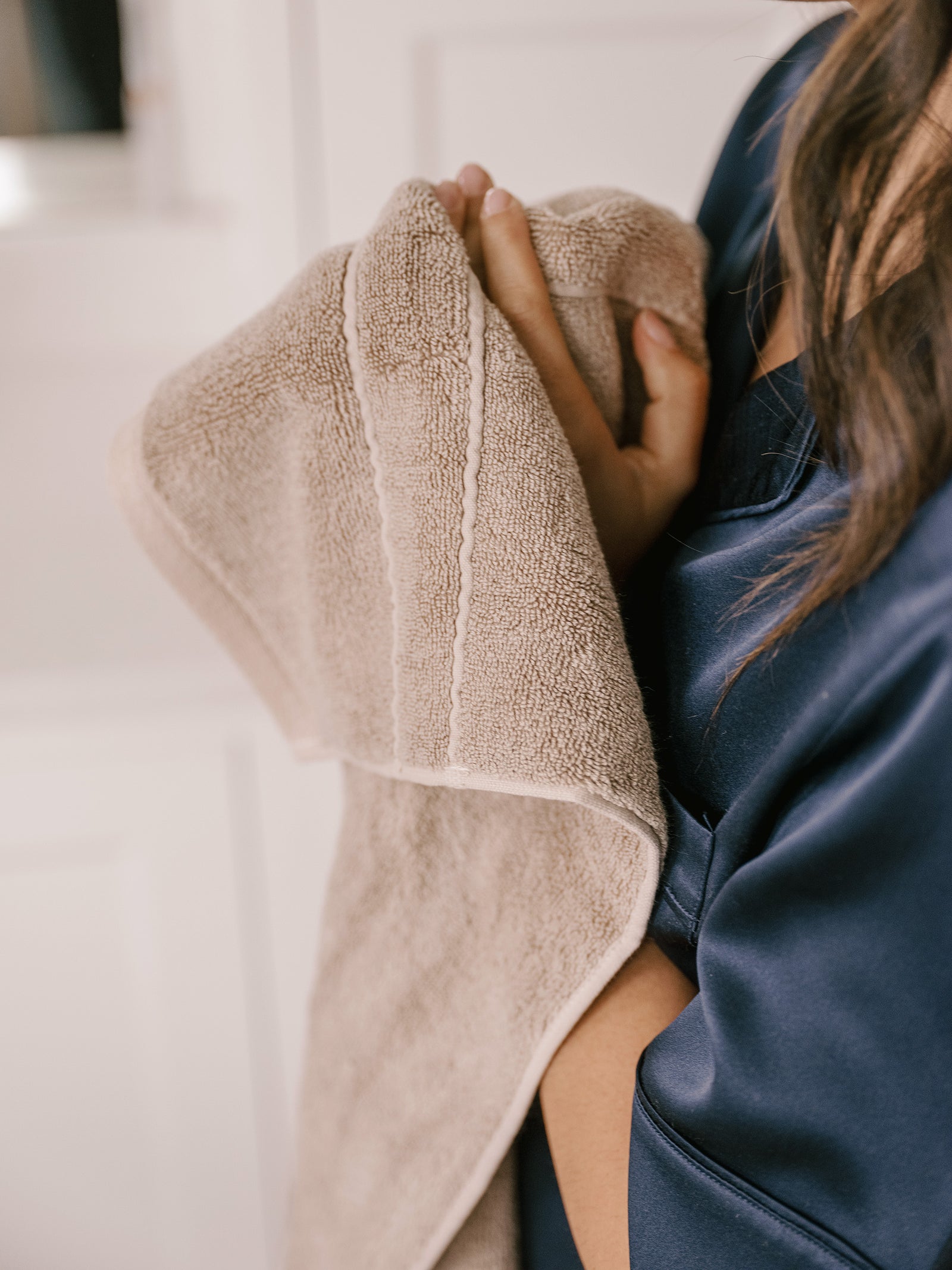 Premium Plush Hand Towels in the color sand. Photo of Premium Plush Hand Towel taken in a bathroom with a woman holding the towel close to her body. 