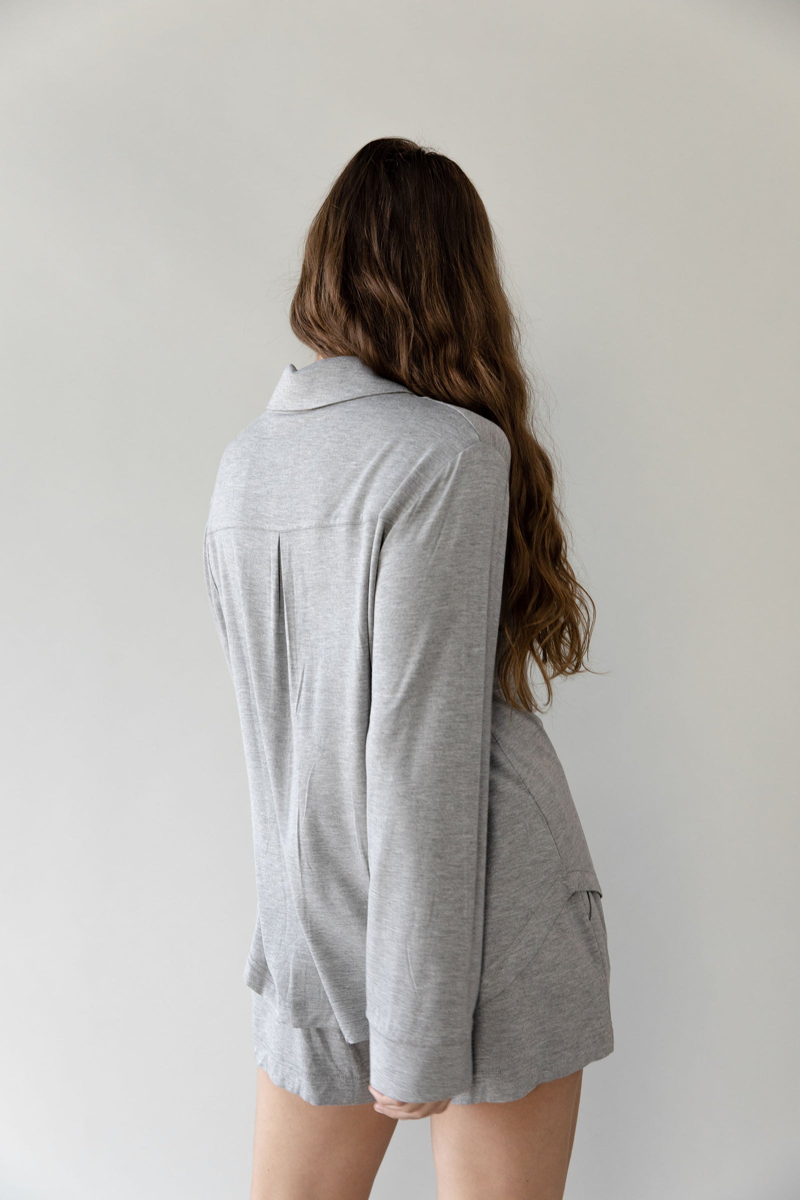 Woman facing backwards wearing a grey Cozy Earth Bamboo Stretch Knit Long Sleeve Polo and shorts on a plain background