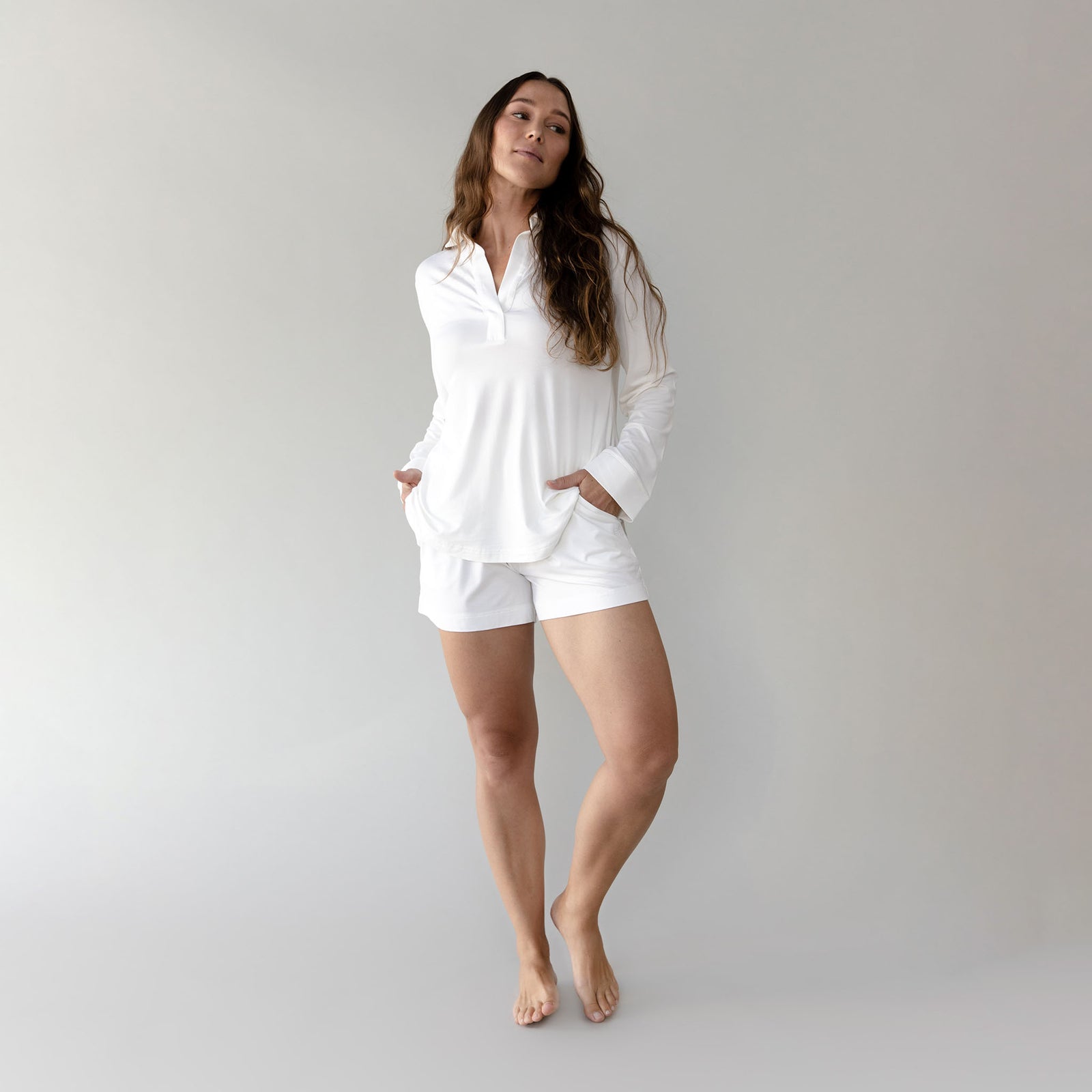 Woman wearing a white Cozy Earth Bamboo Stretch Knit Long Sleeve Polo and shorts on a plain background