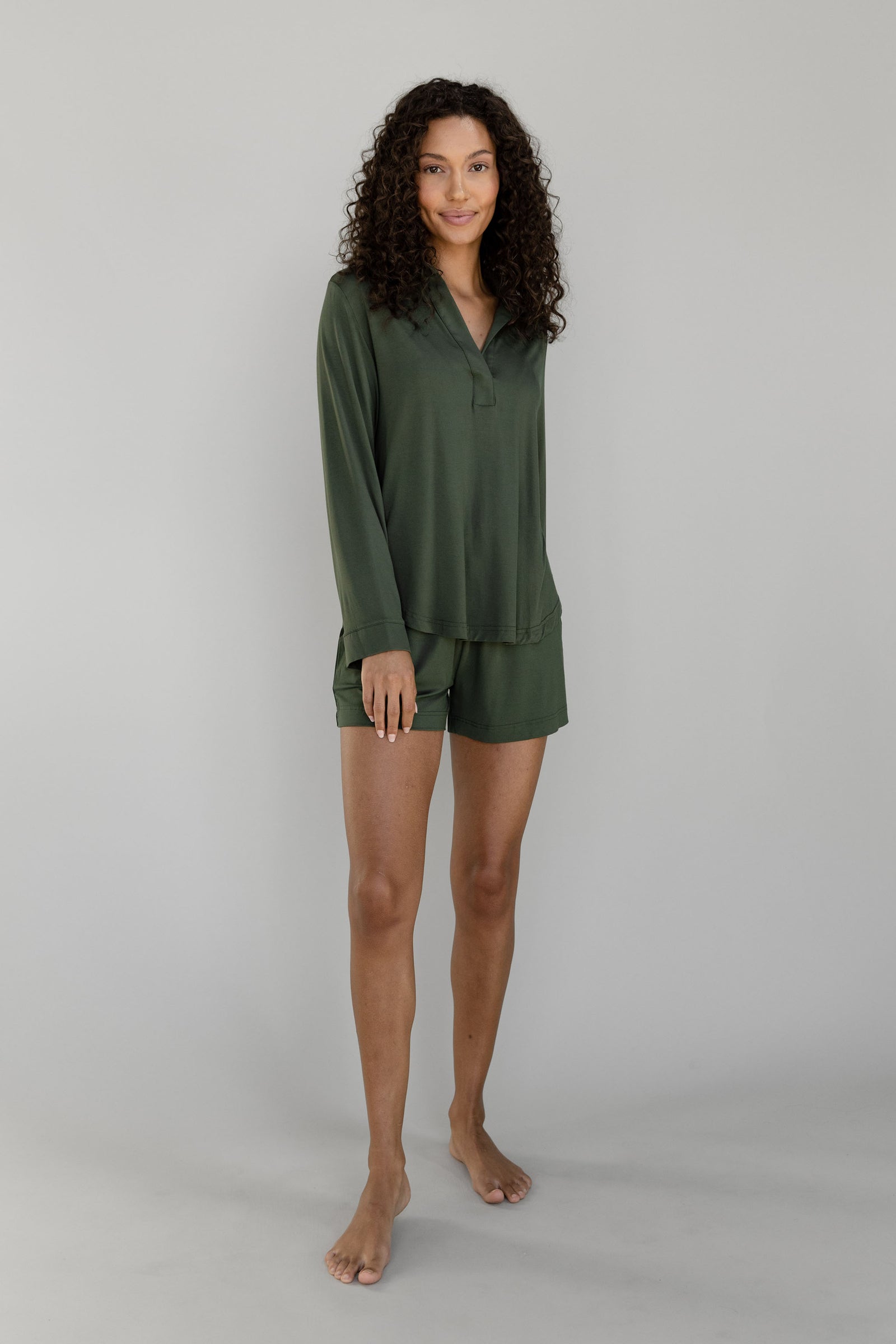 Woman wearing a dark green Cozy Earth Bamboo Stretch Knit Long Sleeve Polo and shorts on a plain background