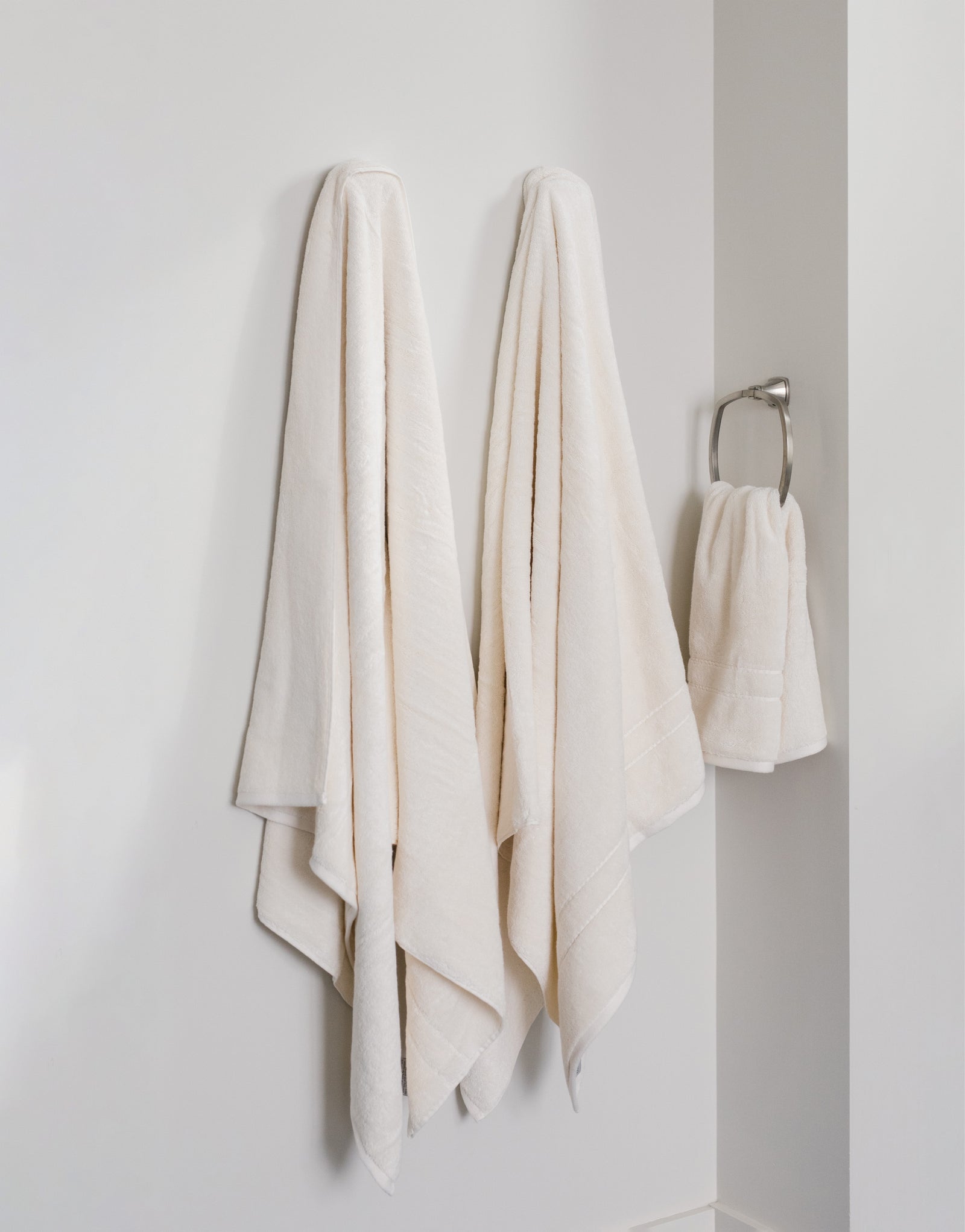 Premium Plush Bath Towels in the color Creme. Photo of Premium Plush Bath Towels taken in a bathroom showing the towels which are hung from a towel rack. 