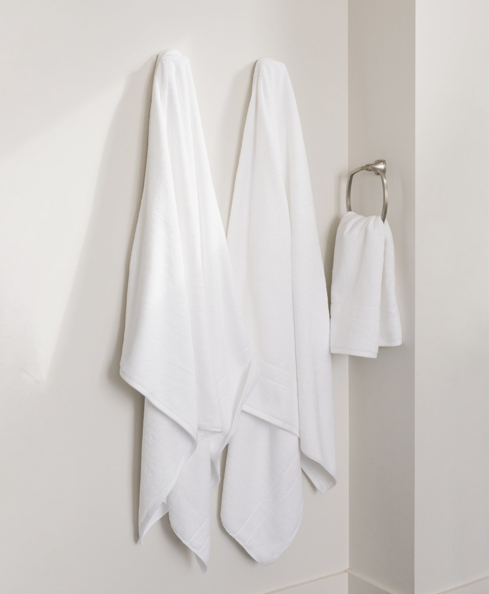Premium Plush Bath Towels in the color white. Photo of Premium Plush Bath Towels taken in a bathroom showing the towels which are hung from a towel rack. 
