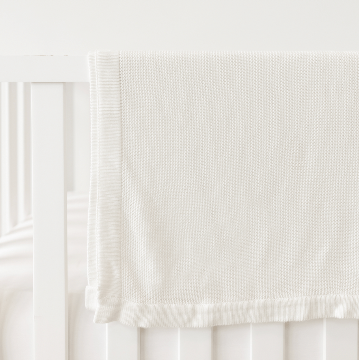 White Cloud Knit Baby Blanket draped over white crib 