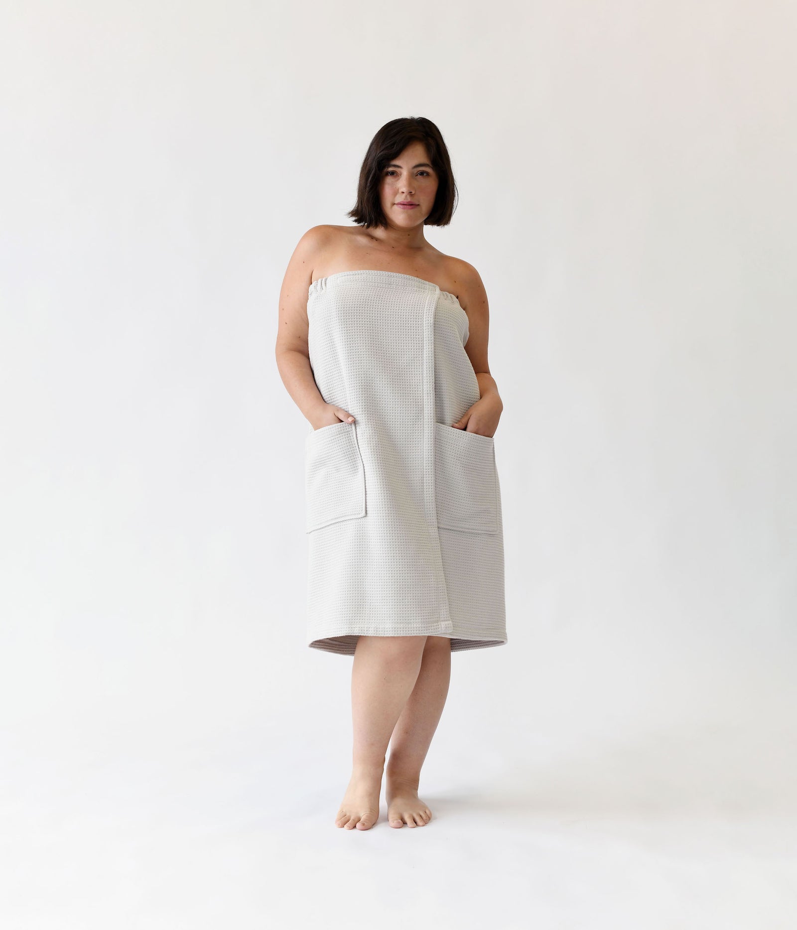 Light Grey Waffle Bath Wrap. The bath wrap is shown being worn by a woman. Photo was taken with a white background.