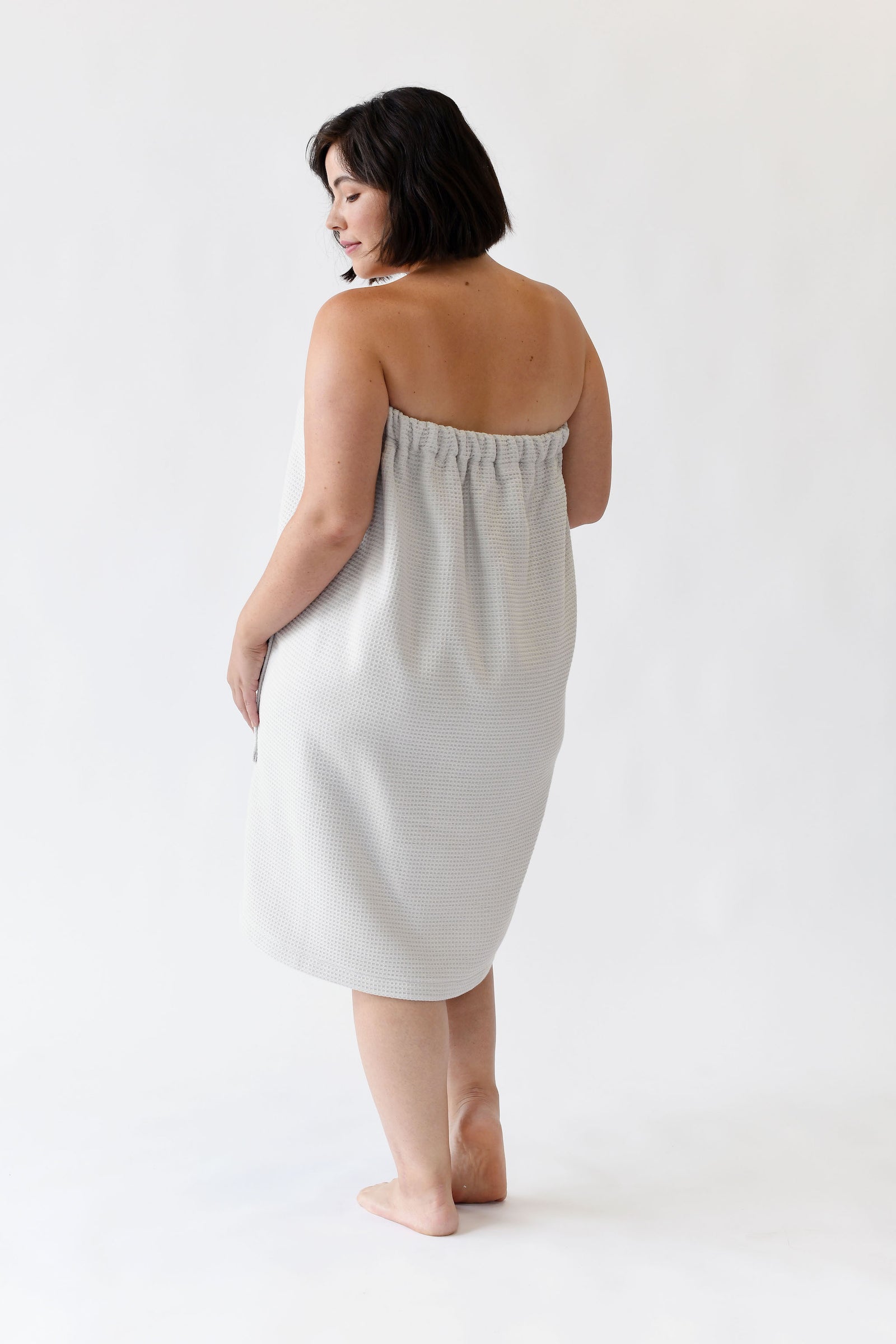Light Grey Waffle Bath Wrap. The bath wrap is shown being worn by a woman. Photo was taken with a white background.