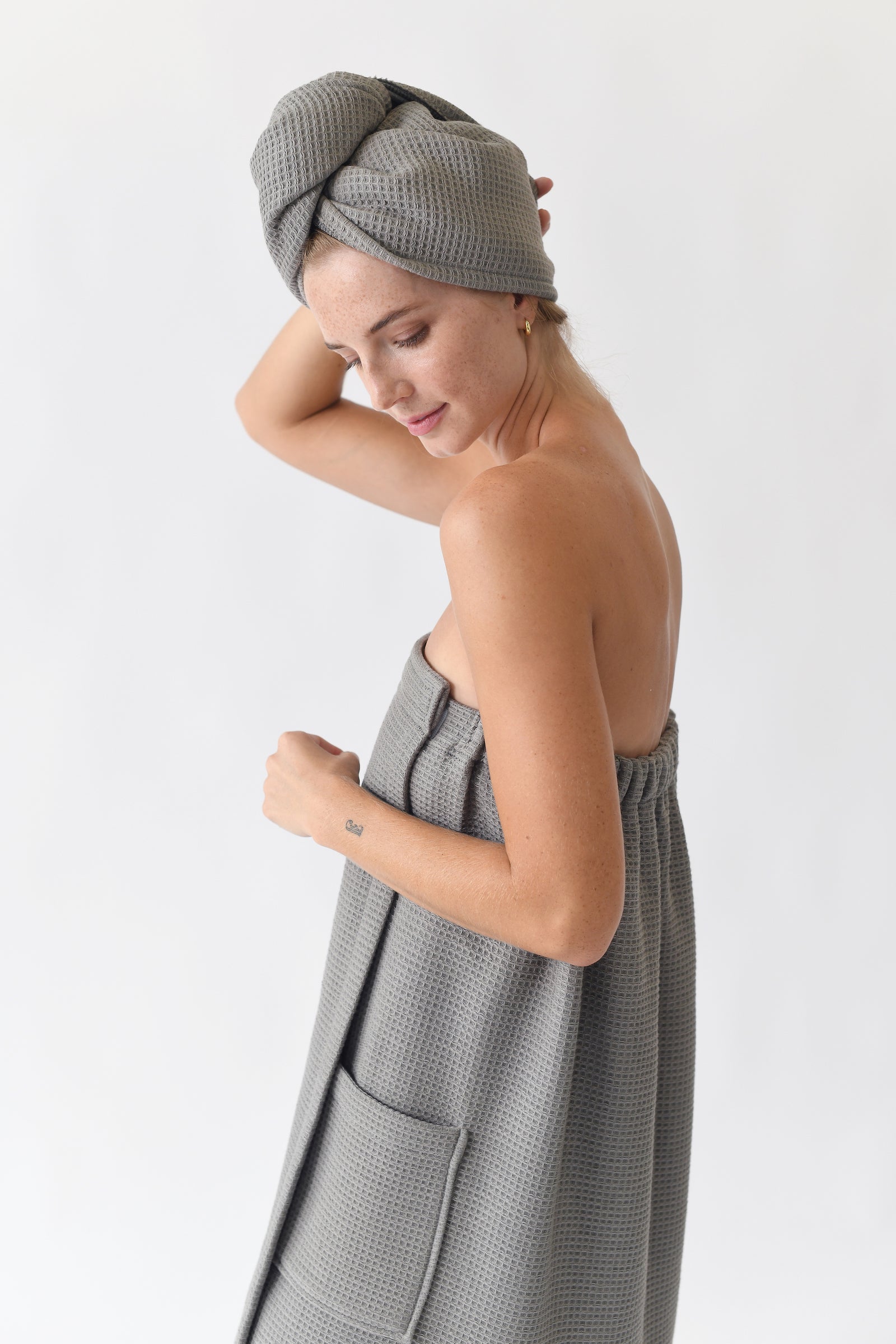 Charcoal Waffle Bath Wrap. The bath wrap is shown being worn by a woman. Photo was taken with a white background.