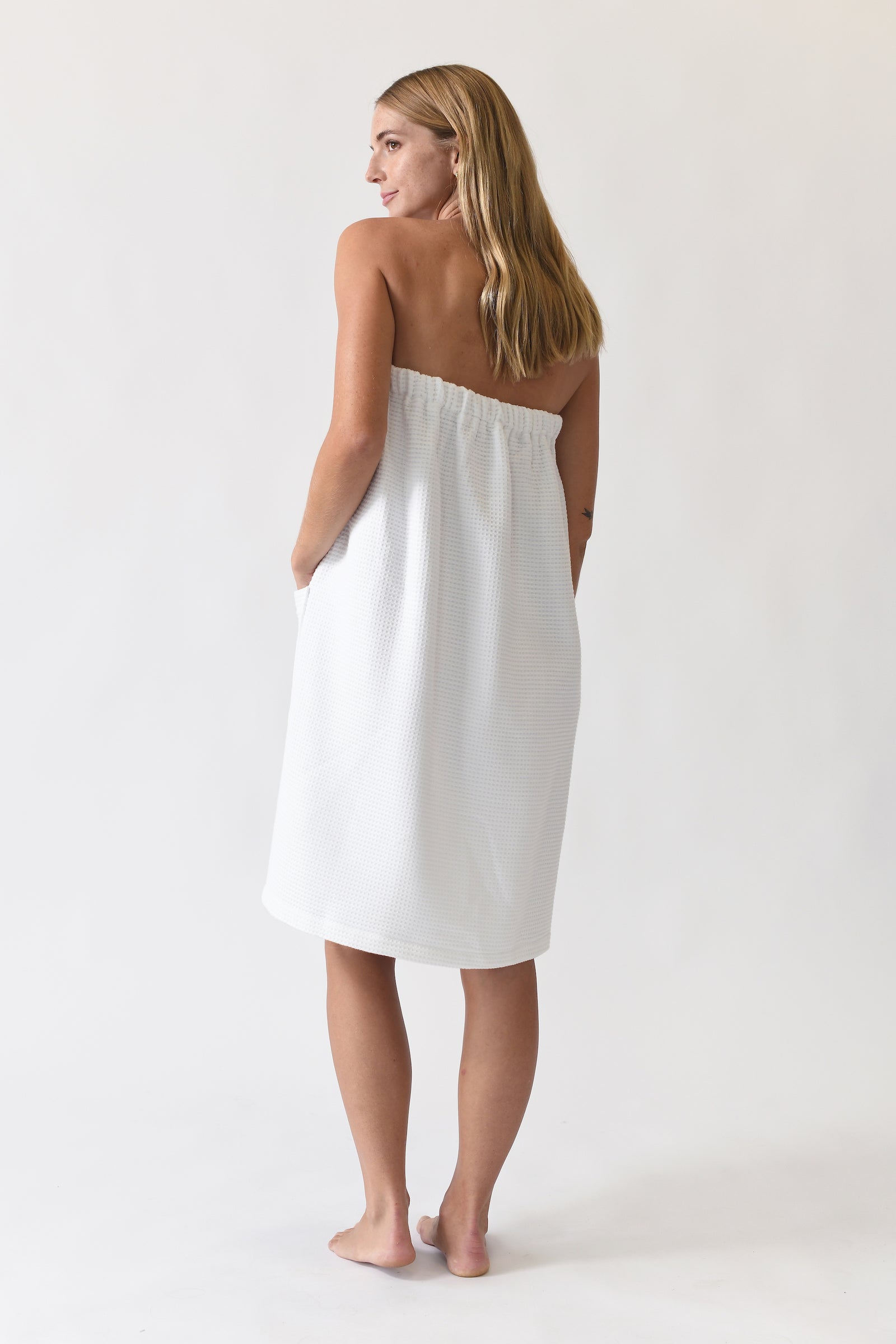 White Waffle Bath Wrap. The bath wrap is shown being worn by a woman. Photo was taken with a white background.