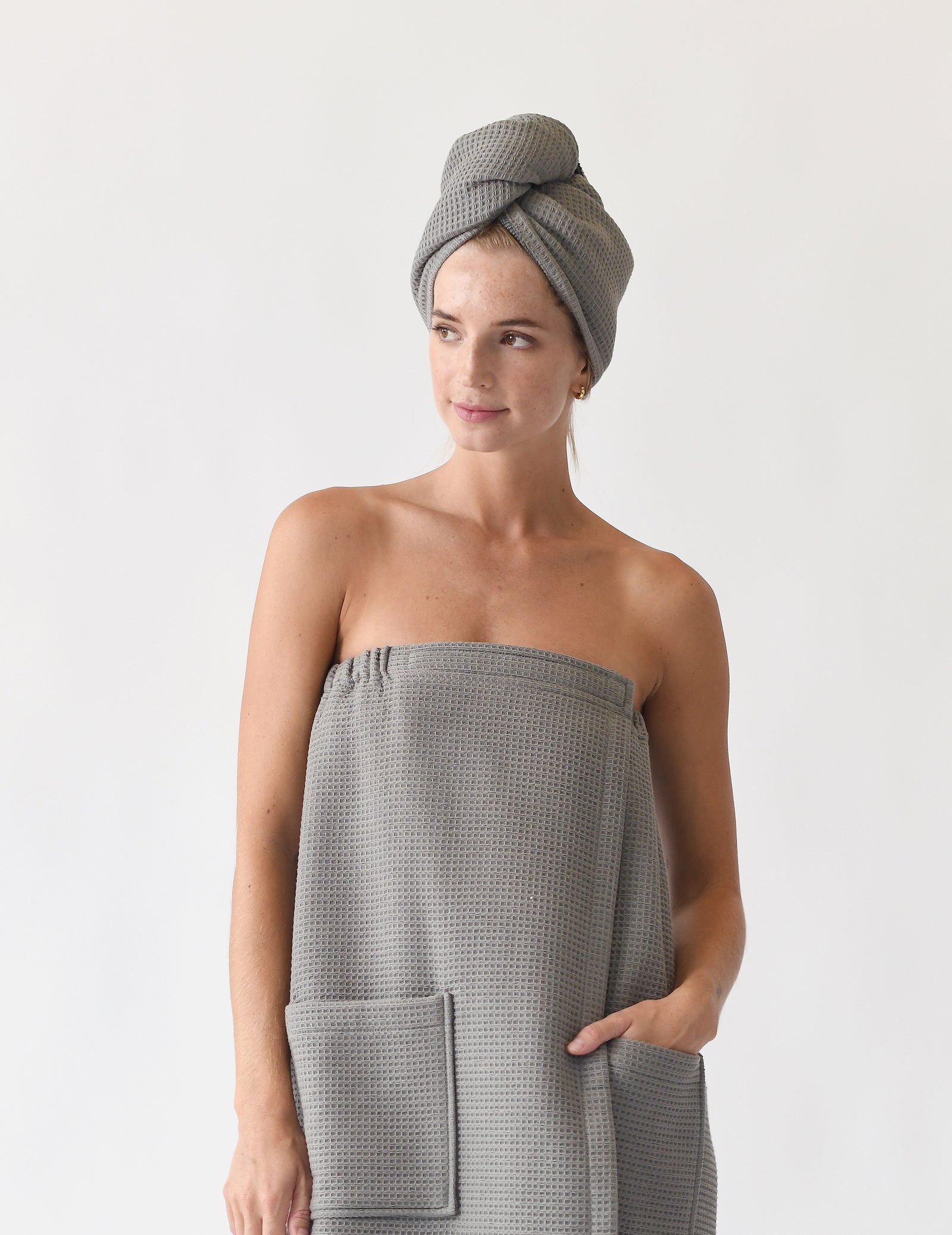 Charcoal Waffle Hair Towel. The hair towel is shown being worn by a woman who is also wearing a waffle bath wrap. Photo was taken with a white background.