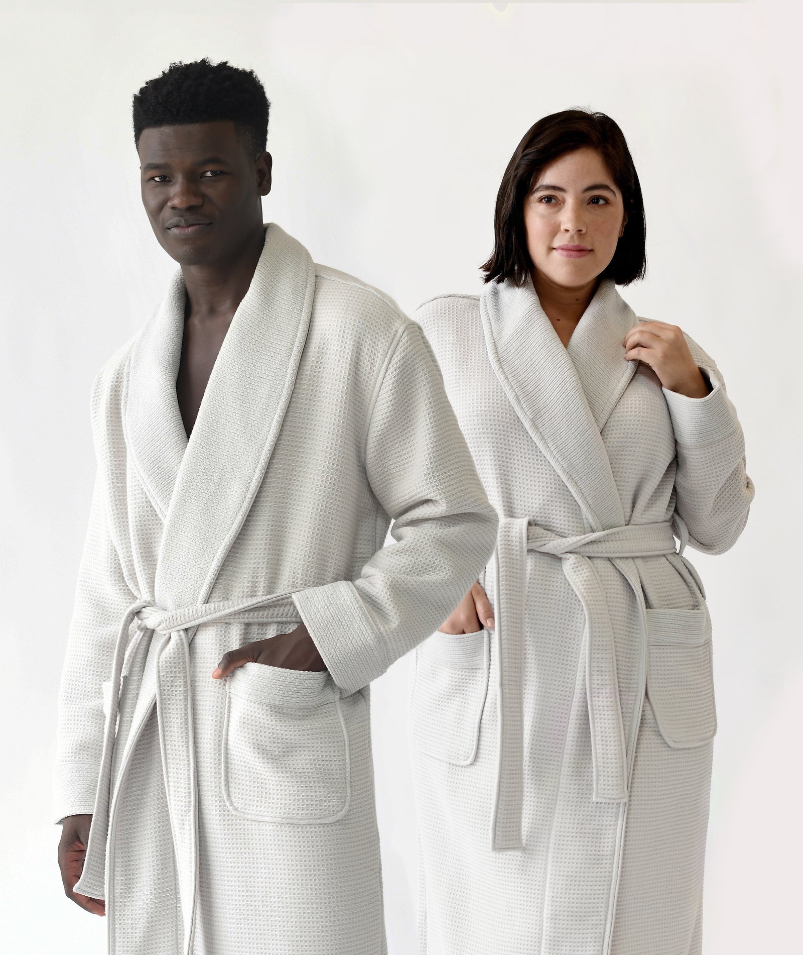  Man and woman standing in front of white background. both the man and the woman are wearing light grey bamboo waffle knit robes. 
