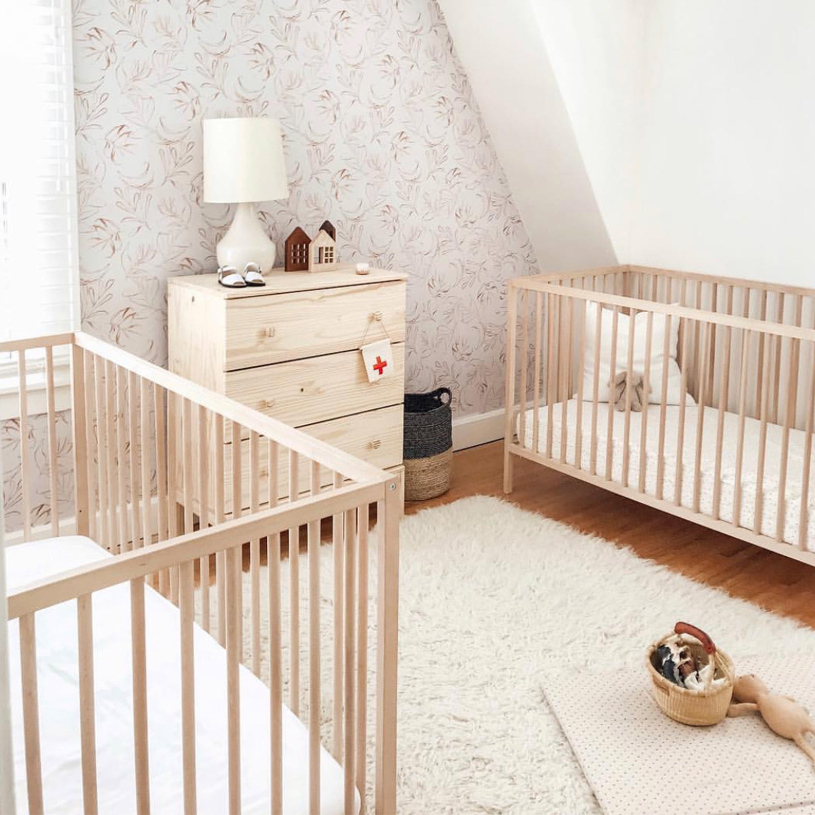 Two wooden cribs with white sheets in a bedroom 