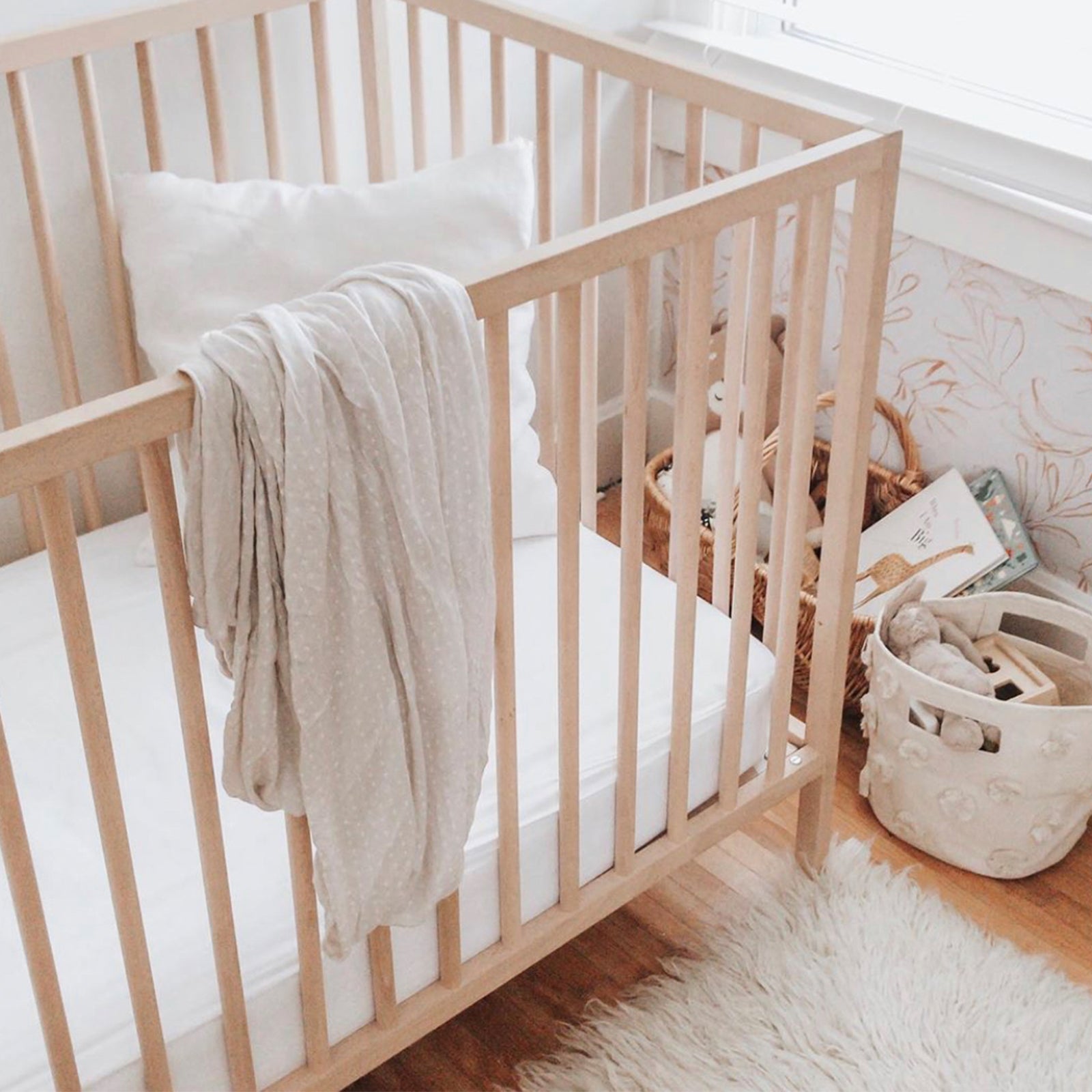 Wooden crib with white sheet with toys in baskets on the ground 