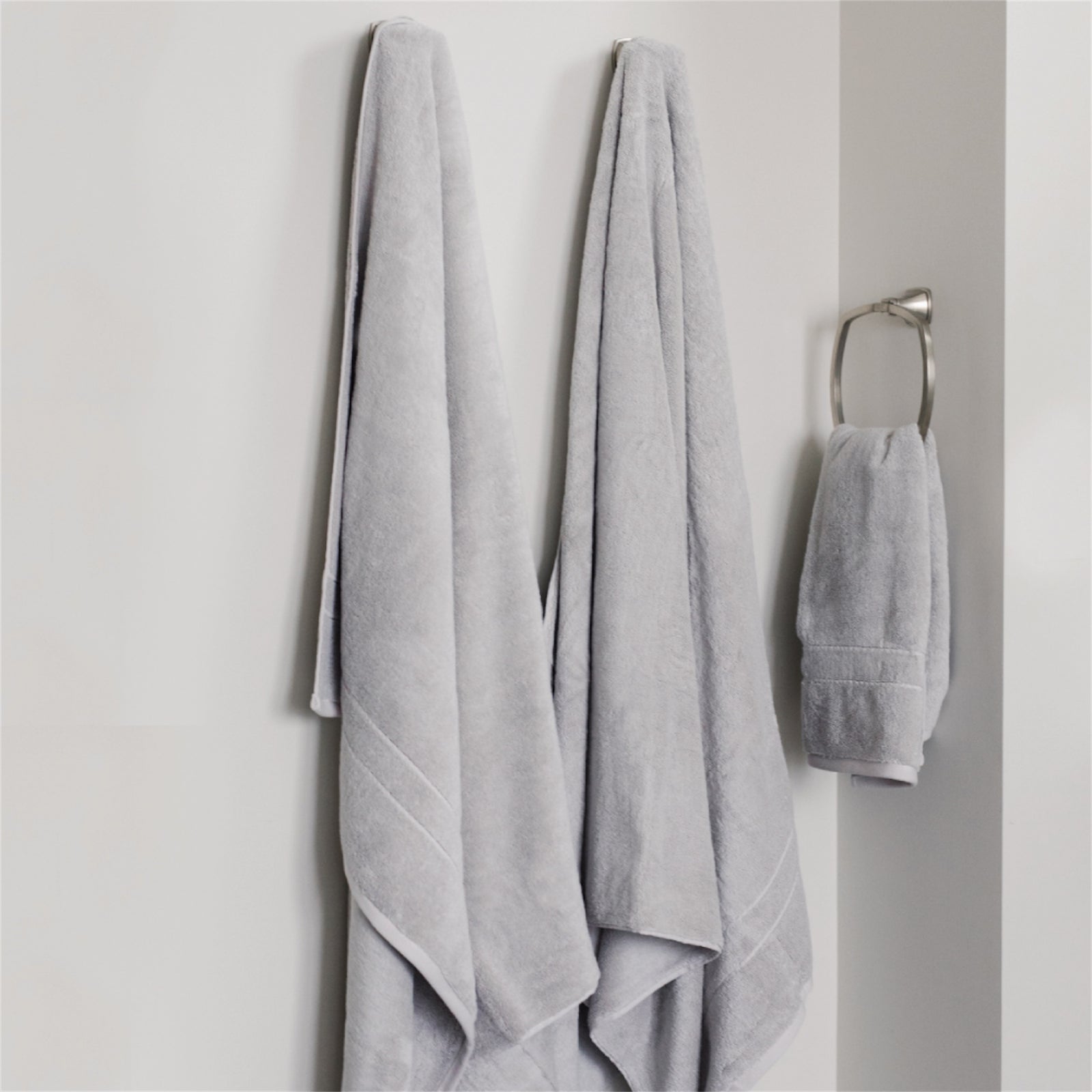 Premium Plush Bath Towels in the color Light Grey. Photo of Premium Plush Bath Towels taken in a bathroom showing the towels which are hung from a towel rack. 