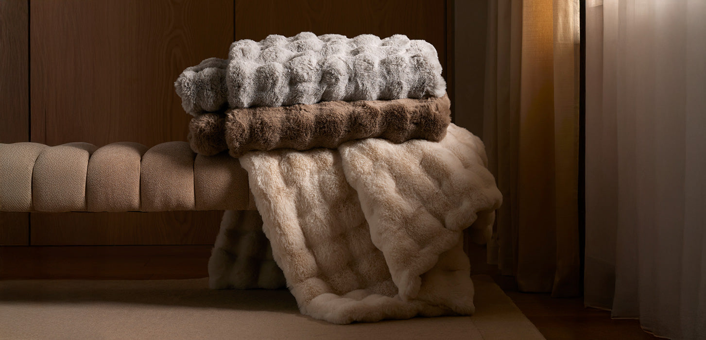 Three bubble cuddle blankets in neutral colors sit on a bench