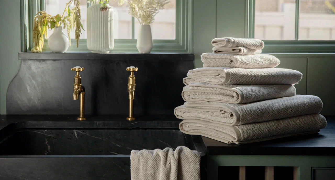  A stack of Cozy Earth towels sits on counter next to a sink with gold faucets.