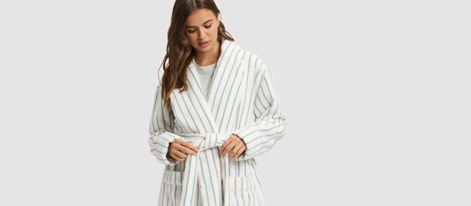 a woman wearing Cozy Earth Striped Luxe Bath Robe stands in front of a grey background