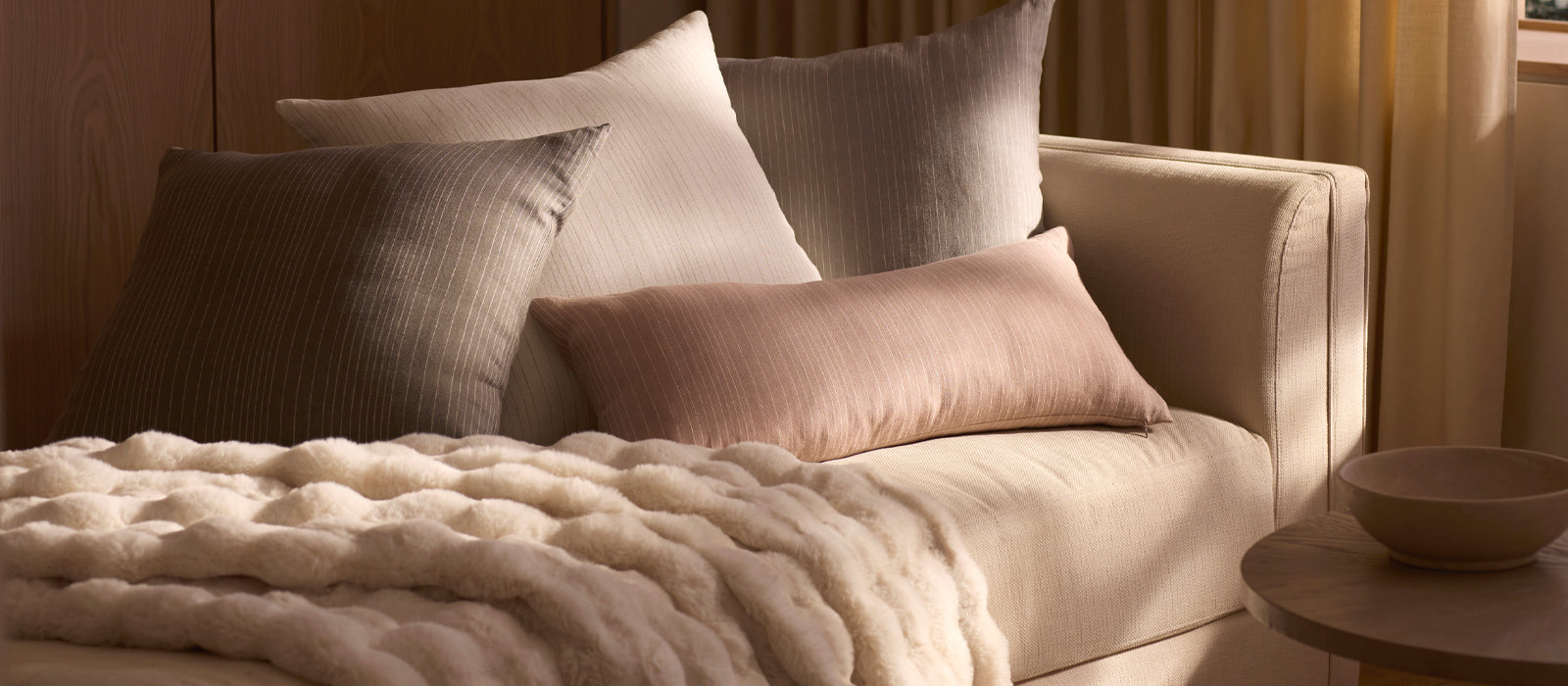 Four throw pillows and a Cozy Earth Bubble Cuddle Blanket sit on a couch in warm, ambient lighting