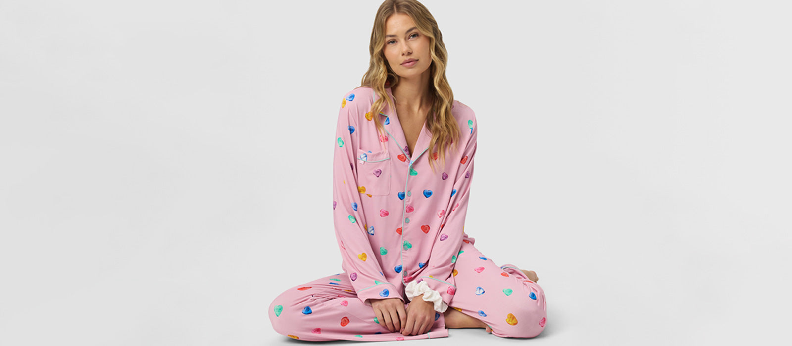 A woman wearing pink Cozy Earth Bamboo Stretch Knit Pajamas with a heart print sits 