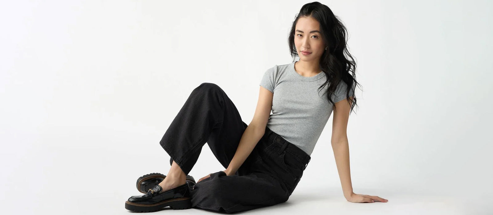 A woman sits with one knee propped up wearing Cozy Earth Fine Ribbed Tee in Grey