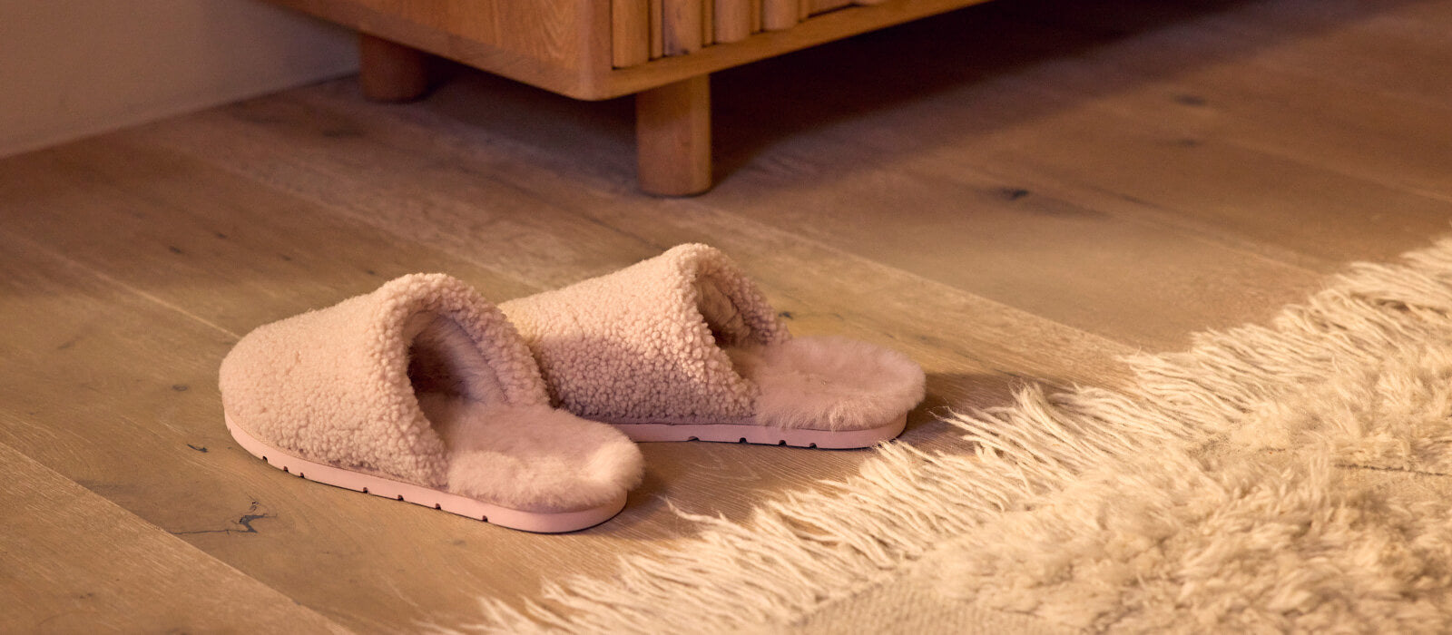 Pink Cozy Earth Sheep Slippers sit on a wood floor