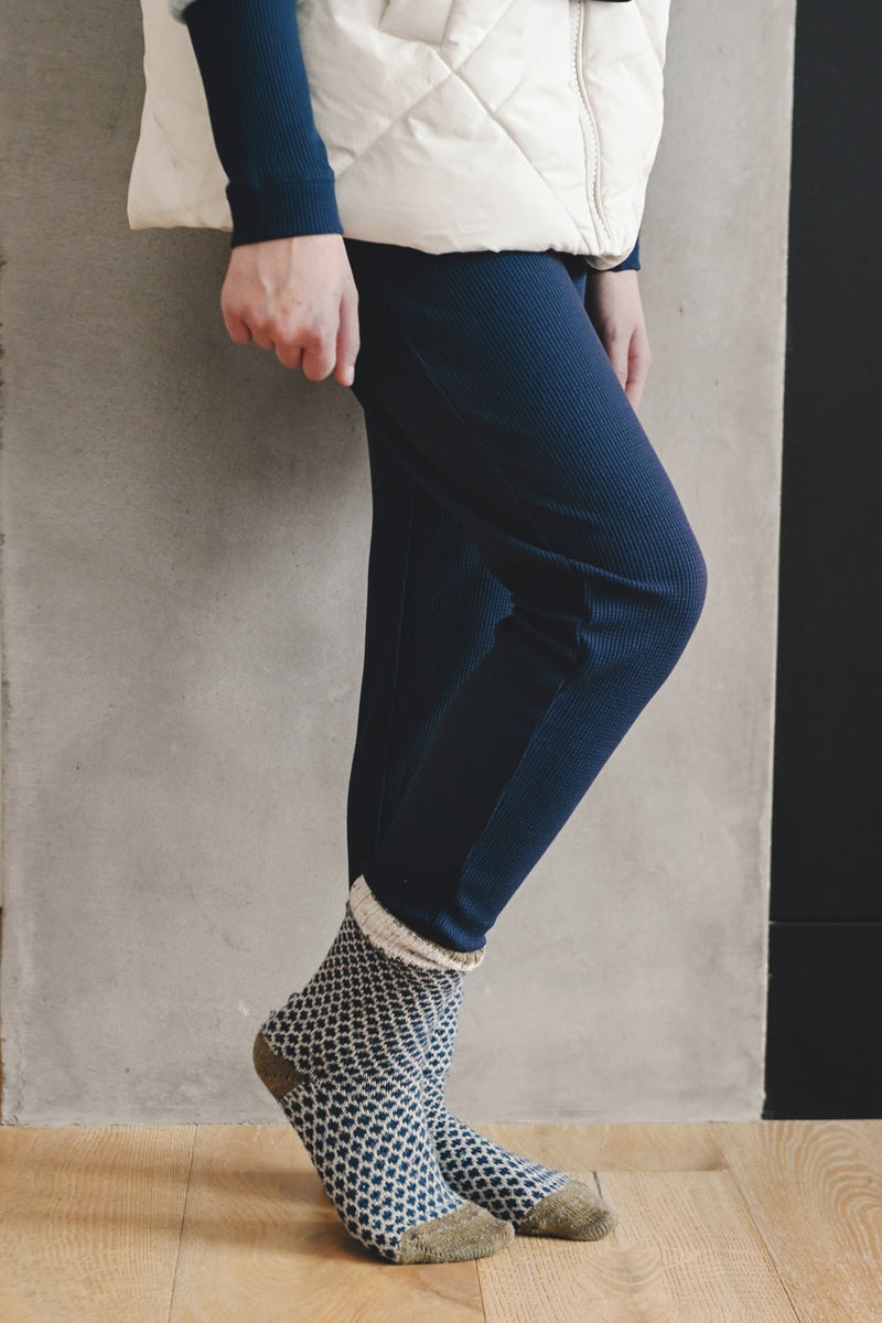 A person wears Cozy Earth Children's Bamboo Waffle Knit Base Layer Pant while standing on a wooden floor in front of a gray wall.