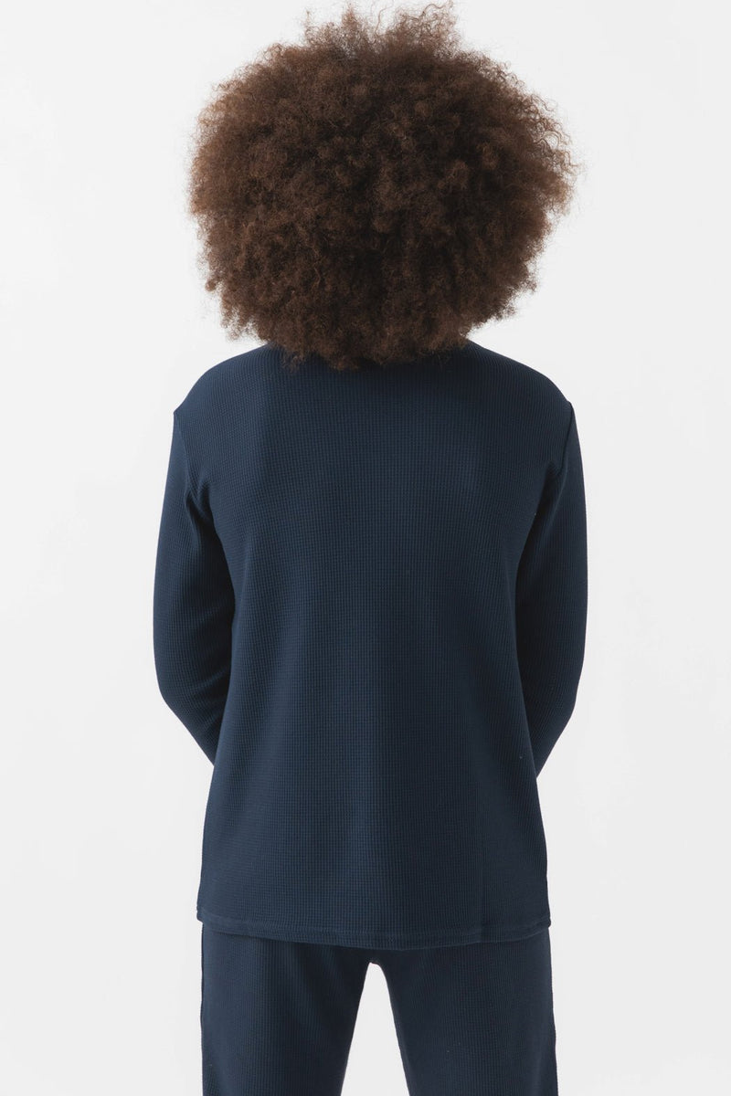 A child with voluminous curly hair, seen from behind, is wearing the Cozy Earth Children's Bamboo Waffle Knit Base Layer Long Sleeve in dark navy. The background is plain white.