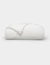 A neatly folded, fluffy Silk Comforter by Cozy Earth is placed against a plain light background. The fabric appears smooth and soft, highlighting its plush and inviting texture.|Filling:Extra