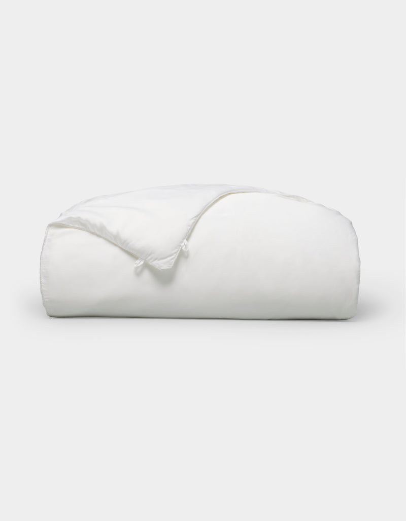 A neatly folded, fluffy Silk Comforter by Cozy Earth is placed against a plain light background. The fabric appears smooth and soft, highlighting its plush and inviting texture.