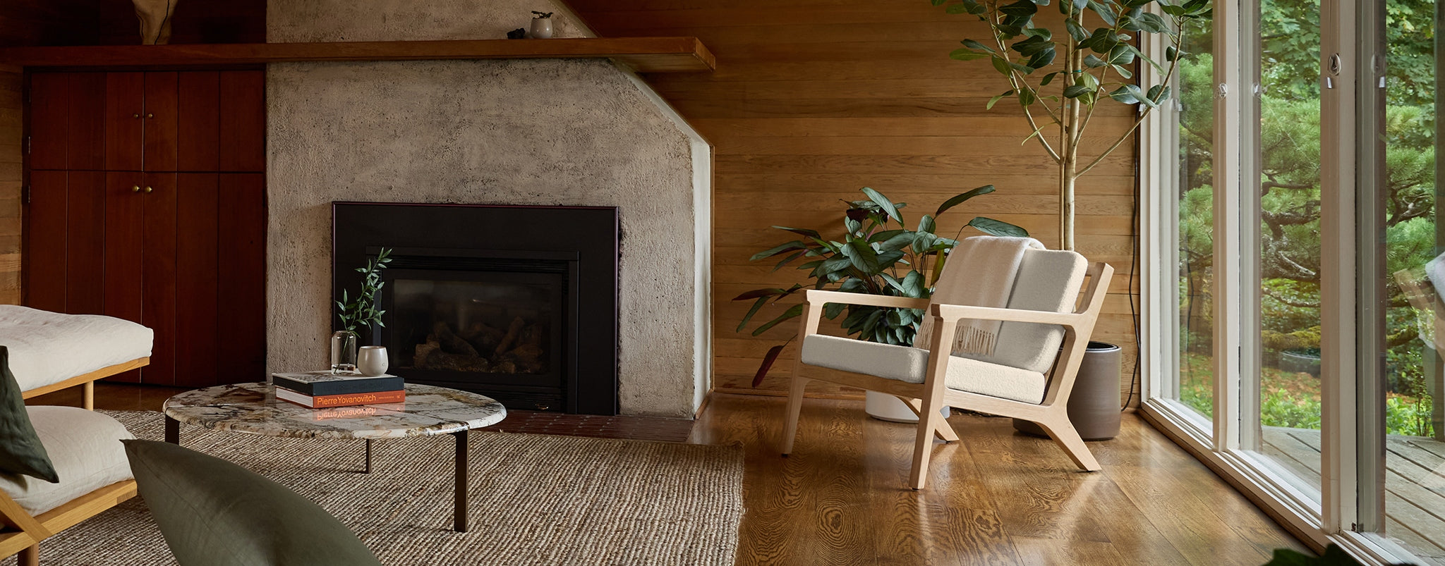 The Cozy Earth Coronado Lounge Chair sits in a room with a concrete fireplace, large windows, jute rug, and wood floors and walls.