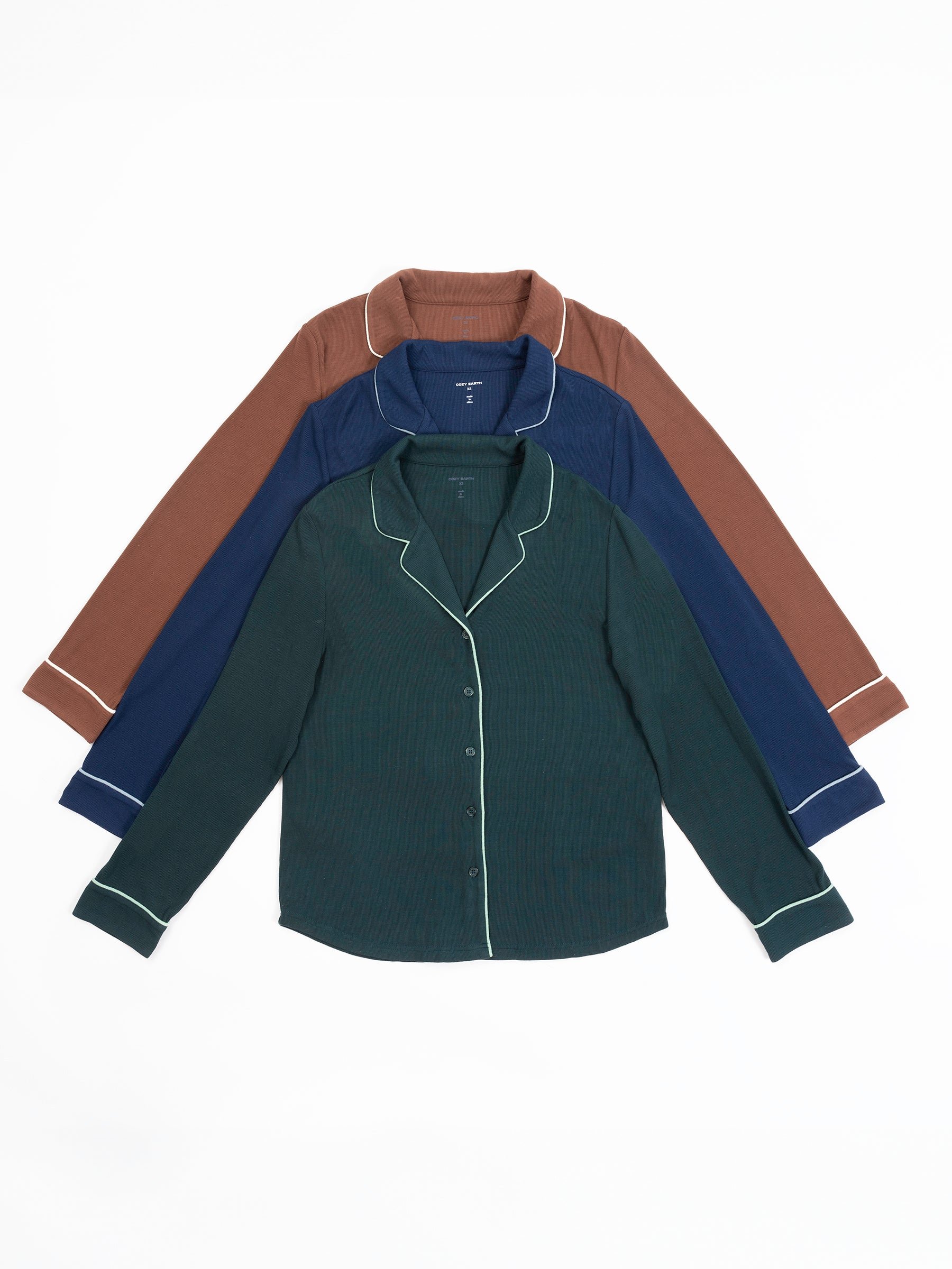 Three Women's Bamboo Rib Knit Classic Long Sleeve Pajama Tops by Cozy Earth are displayed, one on top of the other. The top shirt is dark green with white piping, the middle shirt is navy blue with white piping, and the bottom shirt is brown with white piping. All three have a collar and buttons down the front. 