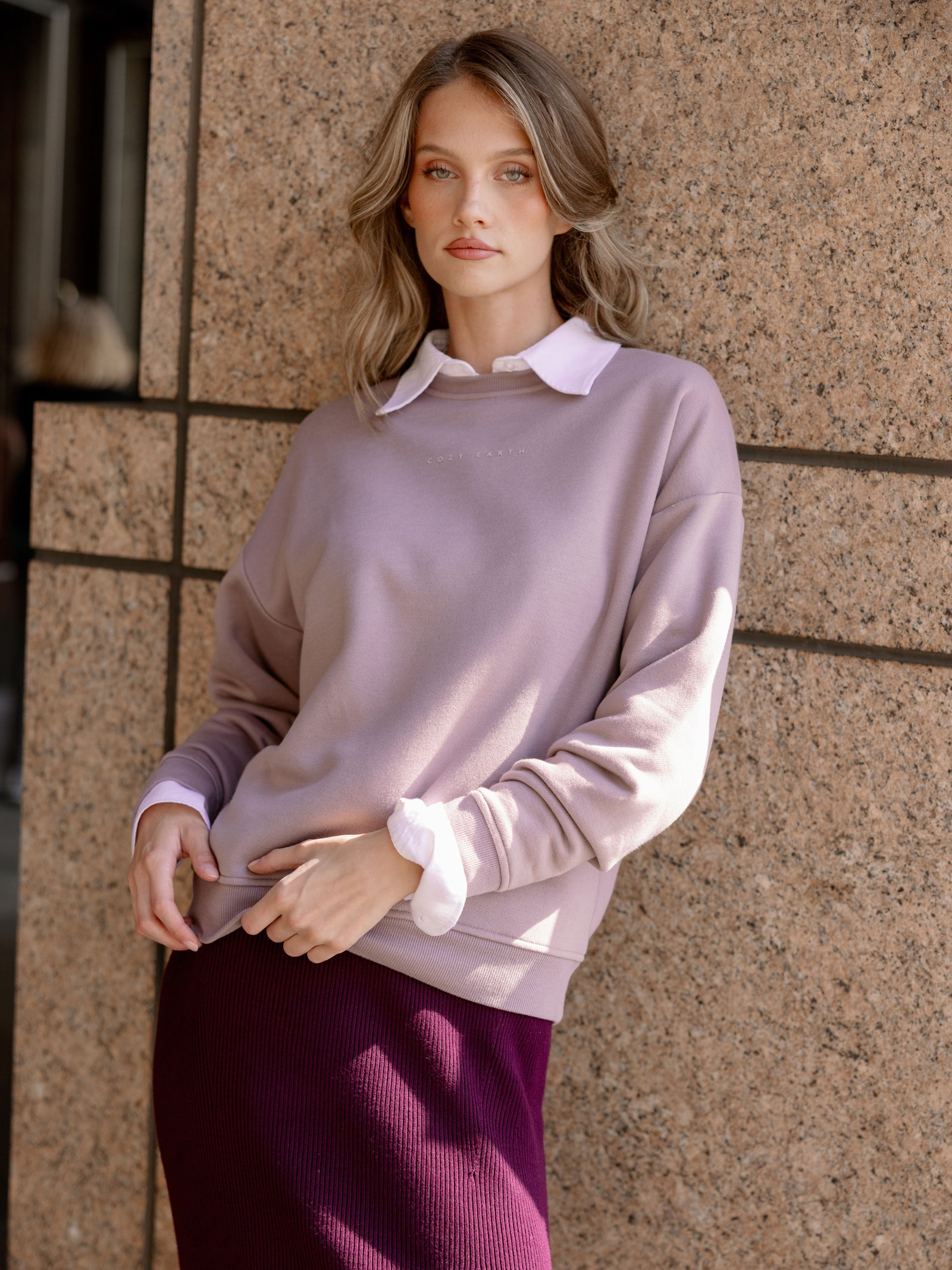 Heather Grey CityScape Pullover Crew. The Pullover is being worn by a female model. An accompanying skirt is being worn to complete the look of the outfit. The photo was taken with a city background. 