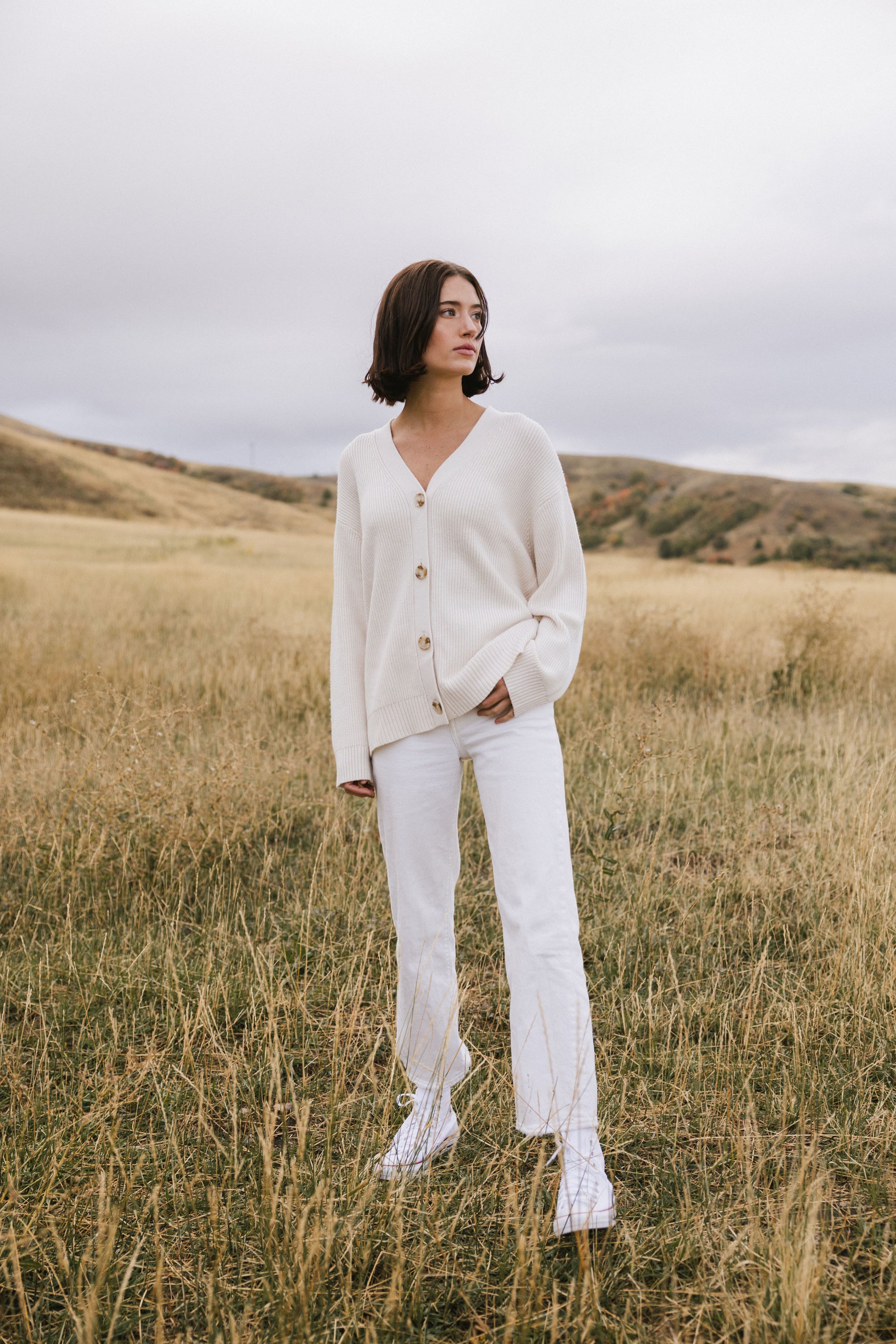 A woman wearing Cozy Earth Classic Cardigan in white stands in a field 