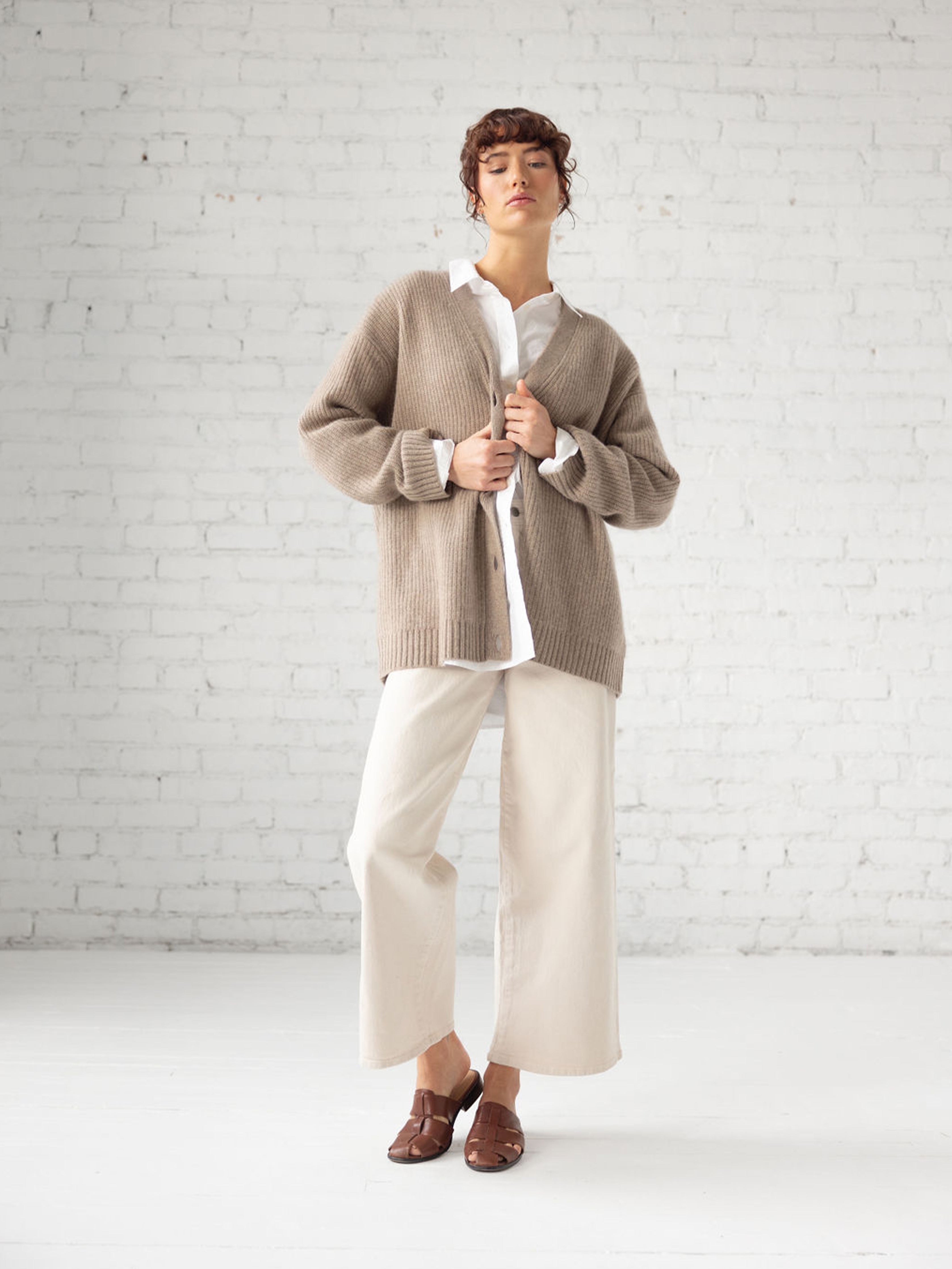 Woman in front of white brick wall wearing almond sunday cardigan |Color:Almond