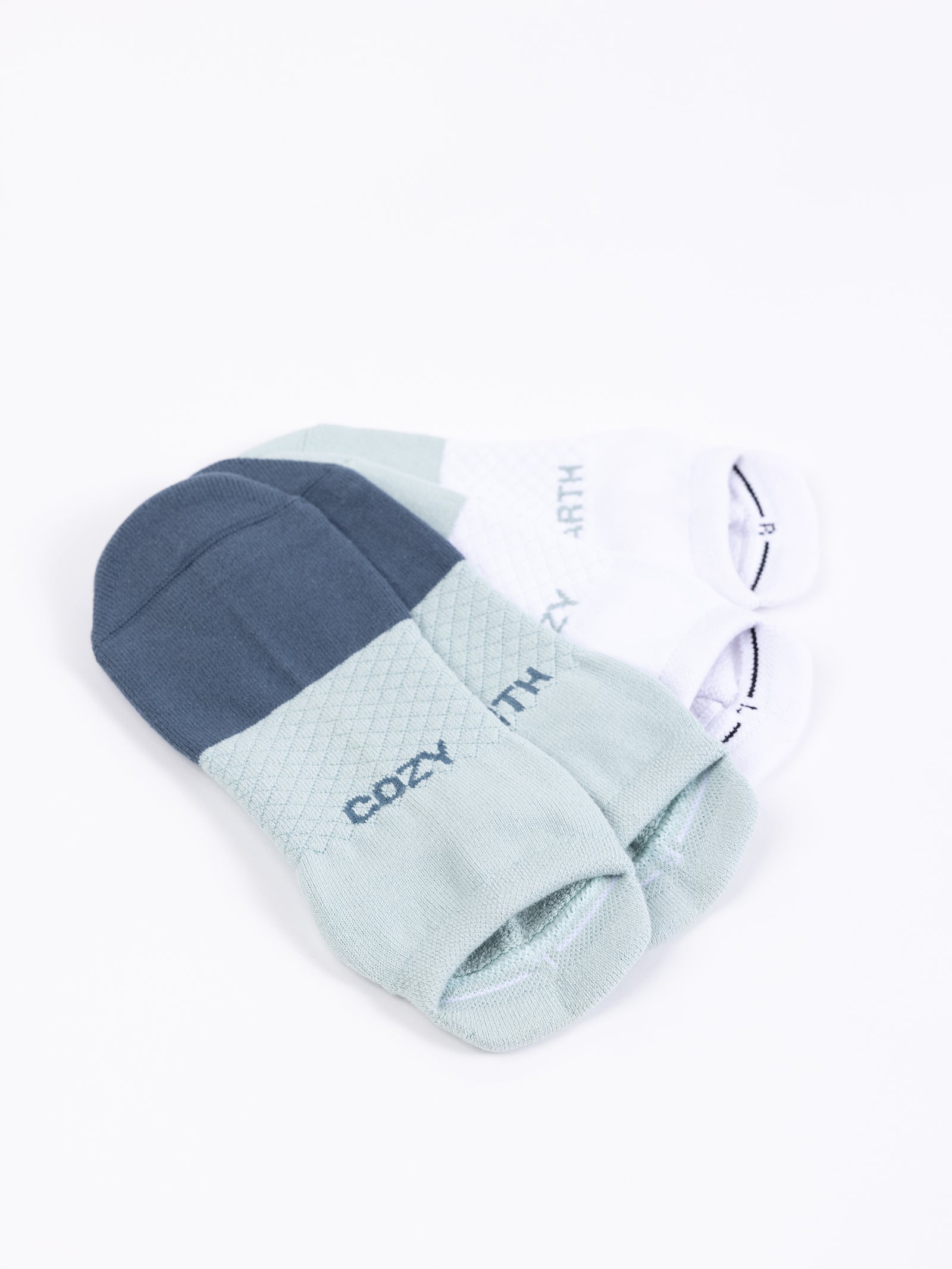 An Essential Ankle Sock 2-Pack from Cozy Earth is displayed. The socks come in shades of blue, green, and white and feature the words "COZY" and "EARTH" on each pair. They also have a subtle textured pattern on the top part. 