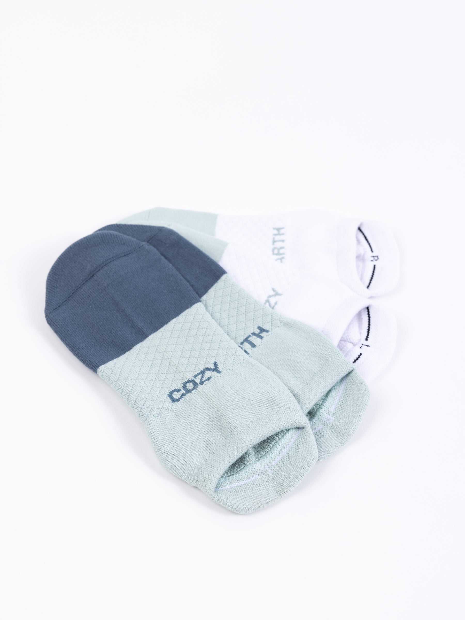 An Essential Ankle Sock 2-Pack from Cozy Earth is displayed. The socks come in shades of blue, green, and white and feature the words "COZY" and "EARTH" on each pair. They also have a subtle textured pattern on the top part. |Color:Arctic