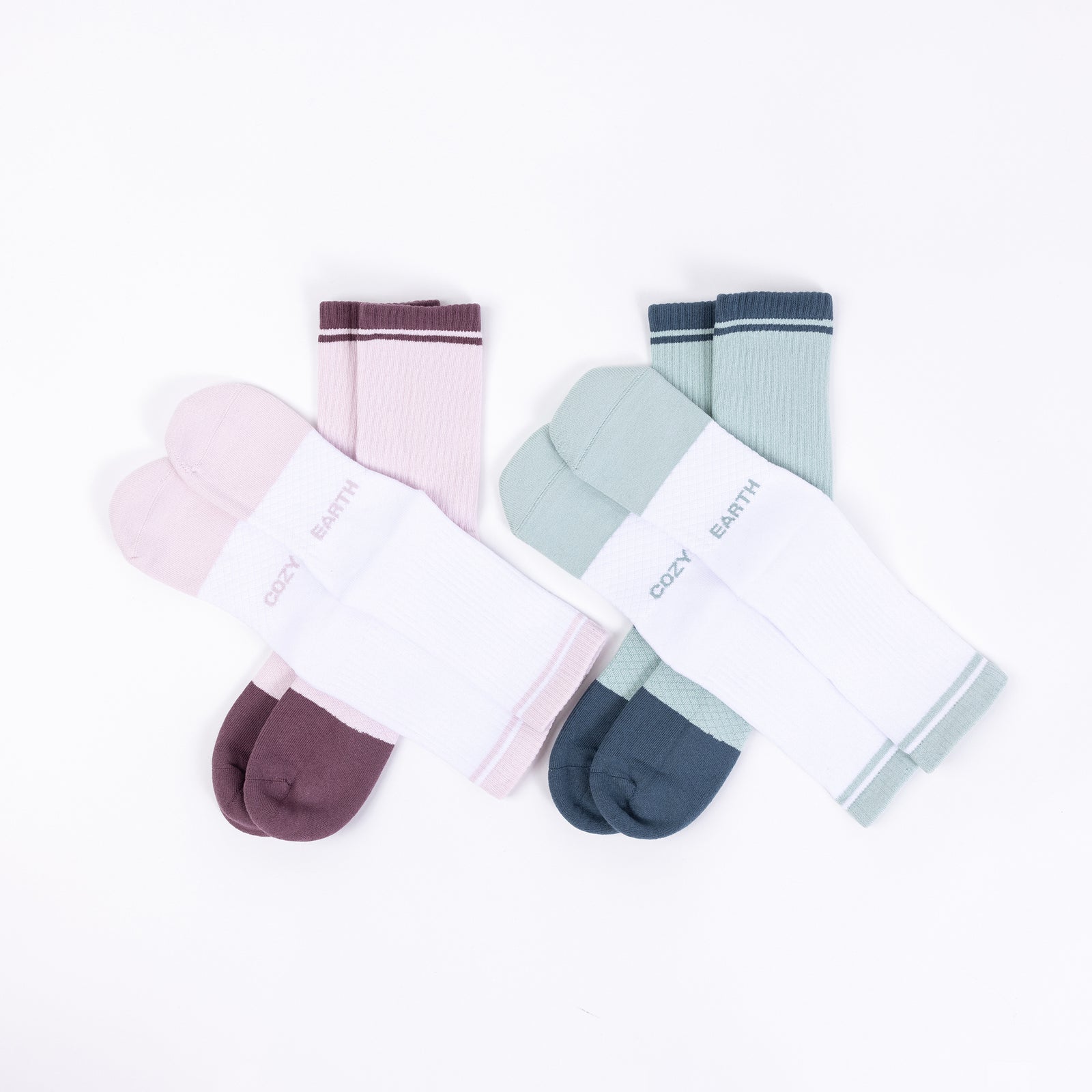 A set of four pairs of Essential Calf Socks from Cozy Earth displayed against a white background. Each pair includes one solid color sock and one white sock with a matching colored stripe at the top. The colors featured are pink, green, dark teal, and an additional vibrant hue. The brand name "COZY EARTH" is clearly visible on each sock. 