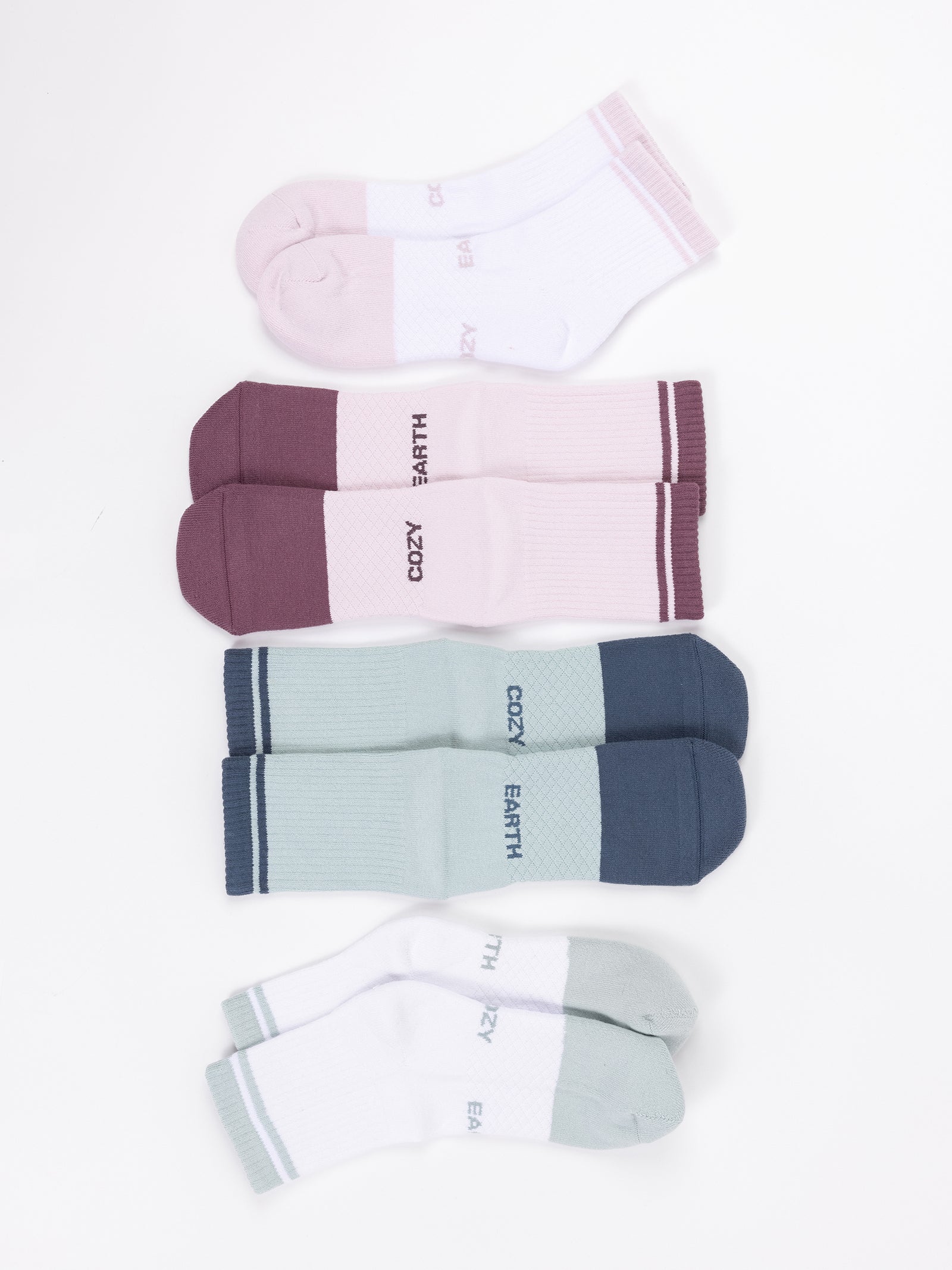 Four pairs from the Essential Quarter Sock 4-Pack by Cozy Earth are laid out. From top to bottom: pink and white ankle socks, maroon and pink crew socks, teal and blue crew socks, and light green and gray ankle socks. Each sock has "COZY EARTH" printed on it. The background is white. 